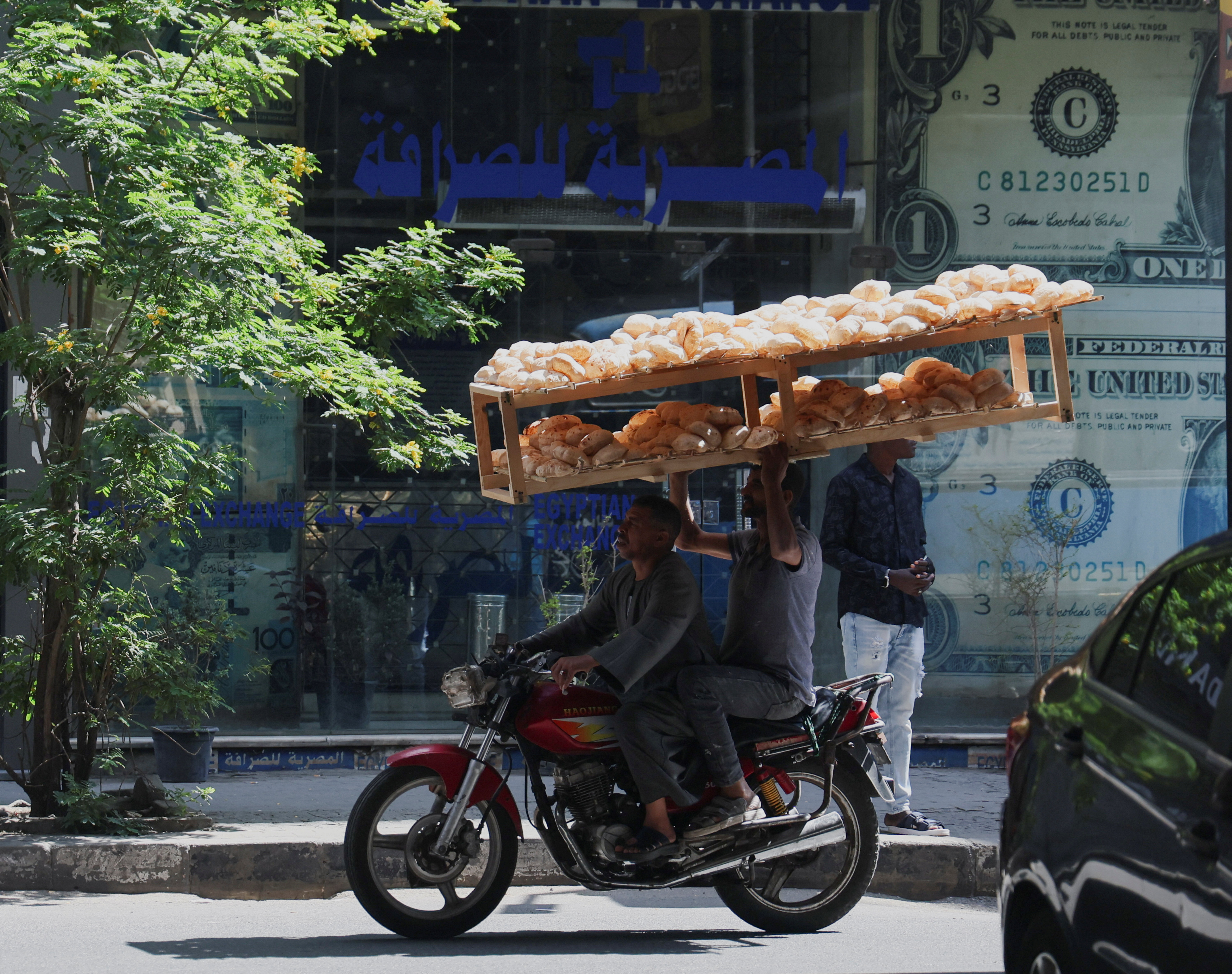 Egyptian street vendors carrying breads, drive past a currency exchange point, displaying images of the U.S. dollar, in Cairo