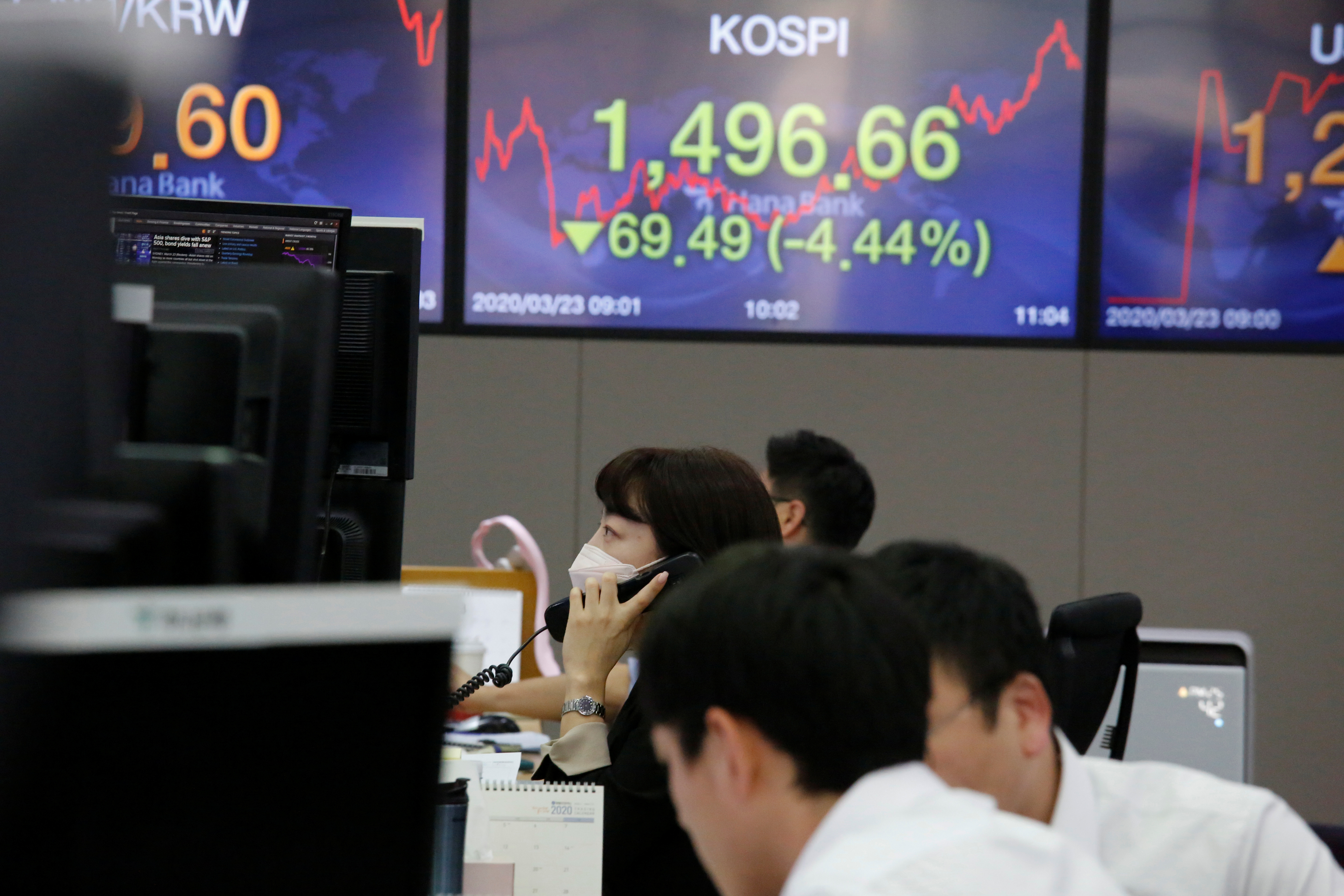 A currency dealer talks on the phone in front of electronic boards showing the Korea Composite Stock Price Index (KOSPI) and the exchange rate between the U.S. dollar and South Korean won, in Seoul