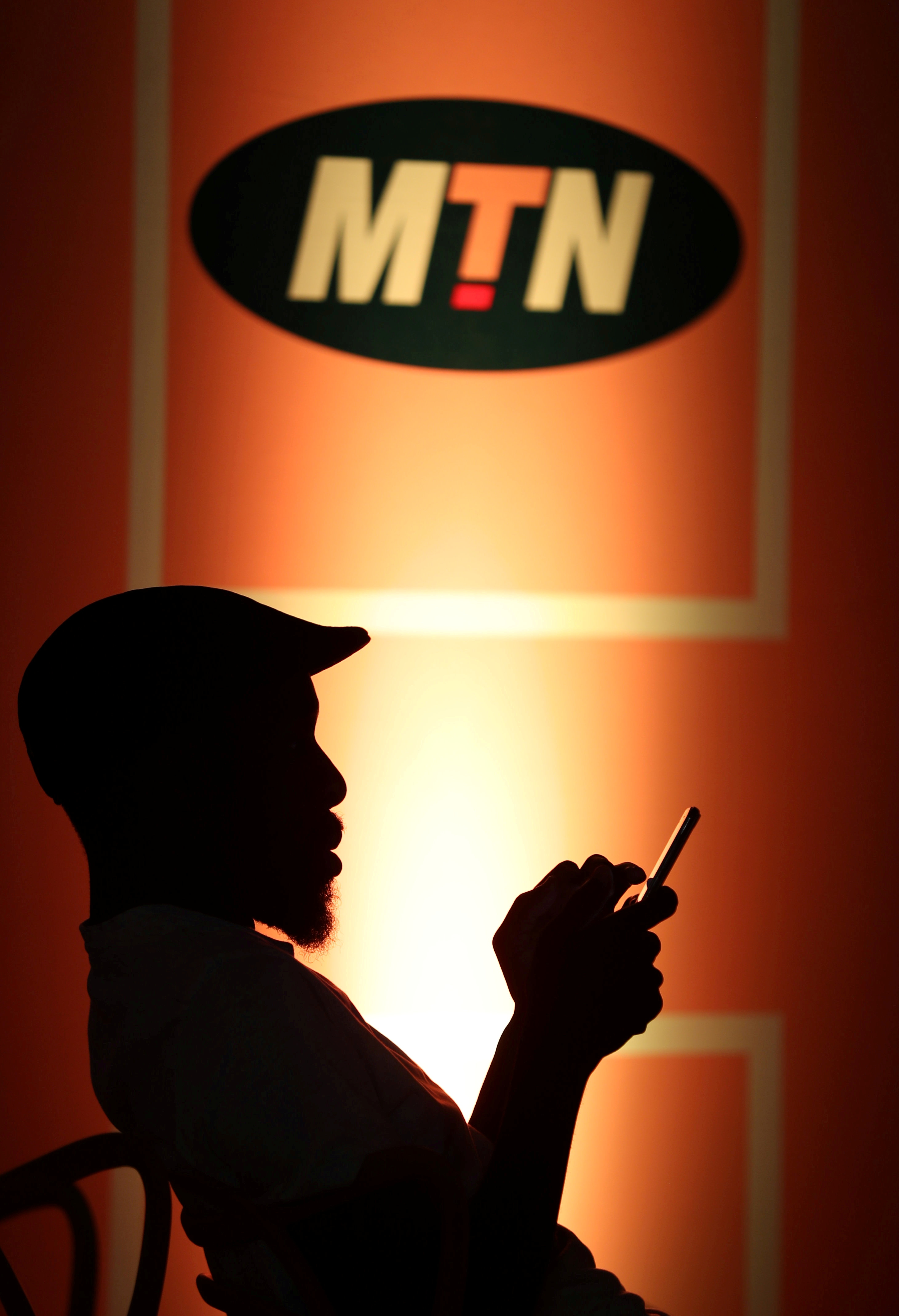 Guest types on his mobile phone as he sits below an MTN logo during the launch of its mobile money service in Johannesburg