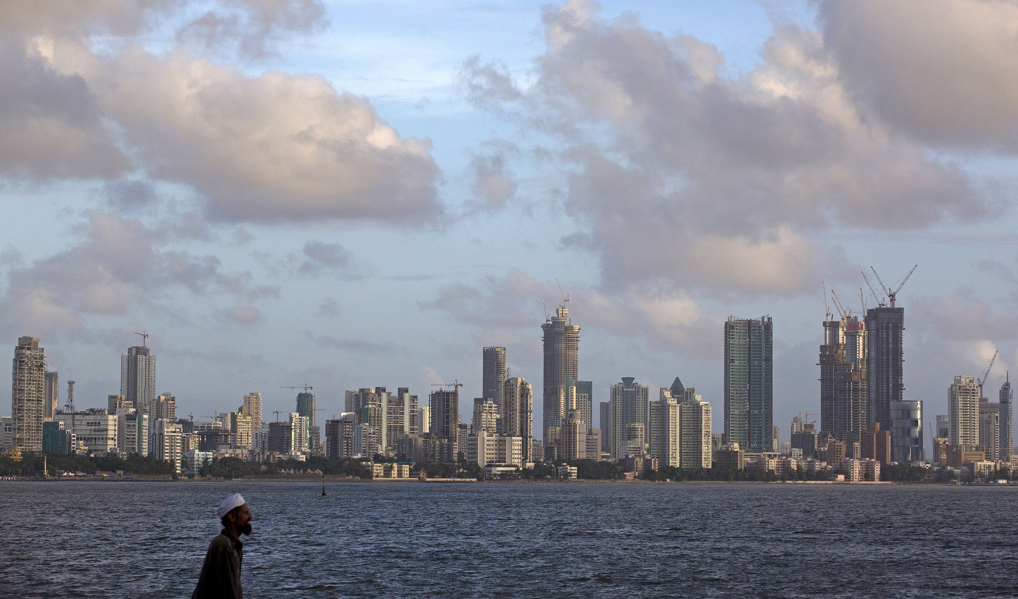 A man walks at the seafront as scattered clouds are seen over Mumbai's skyline
