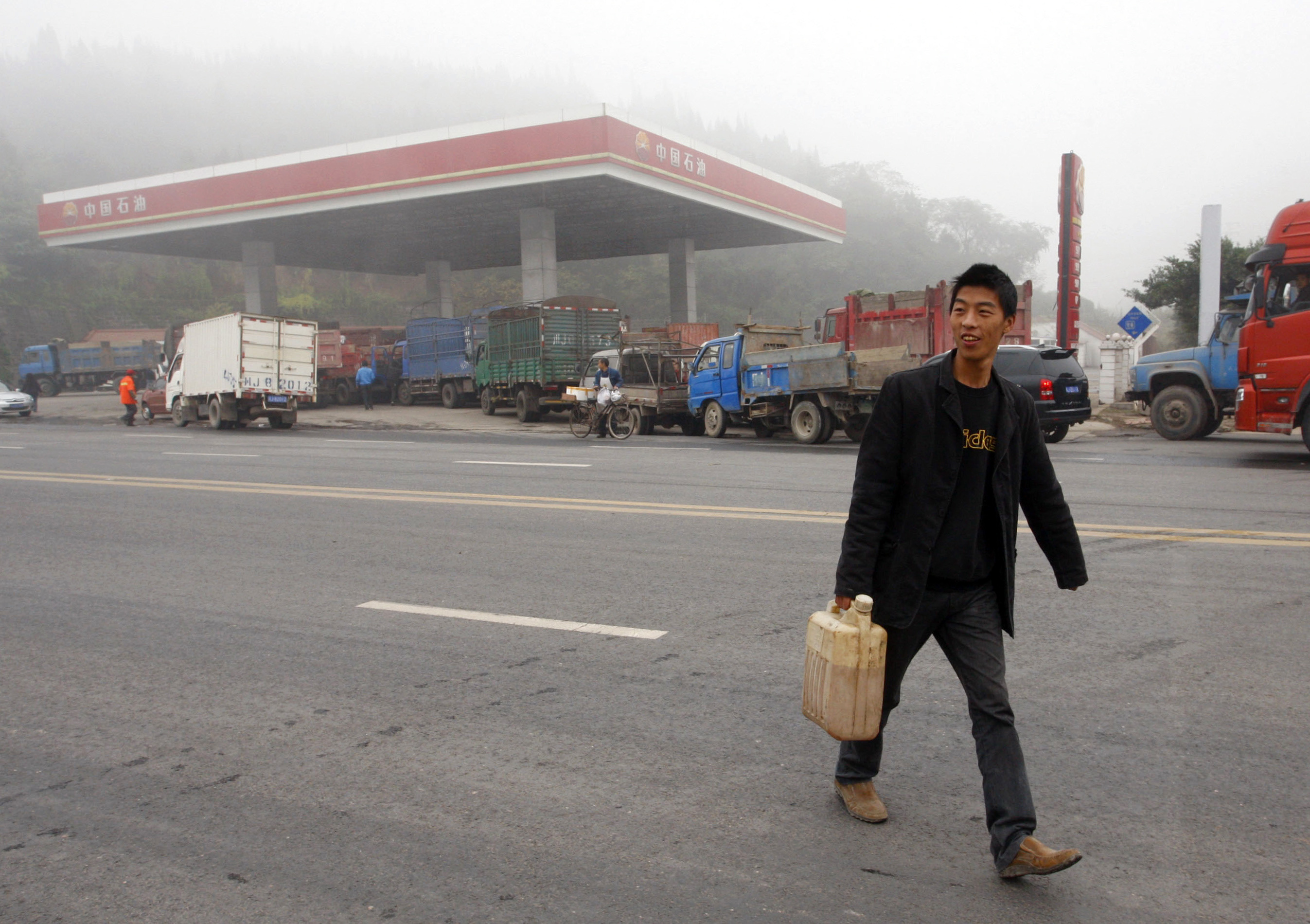 Truck driver carries a canister of diesel as he walks past queued vehicles waiting to fill their tanks at a gas station in Suining