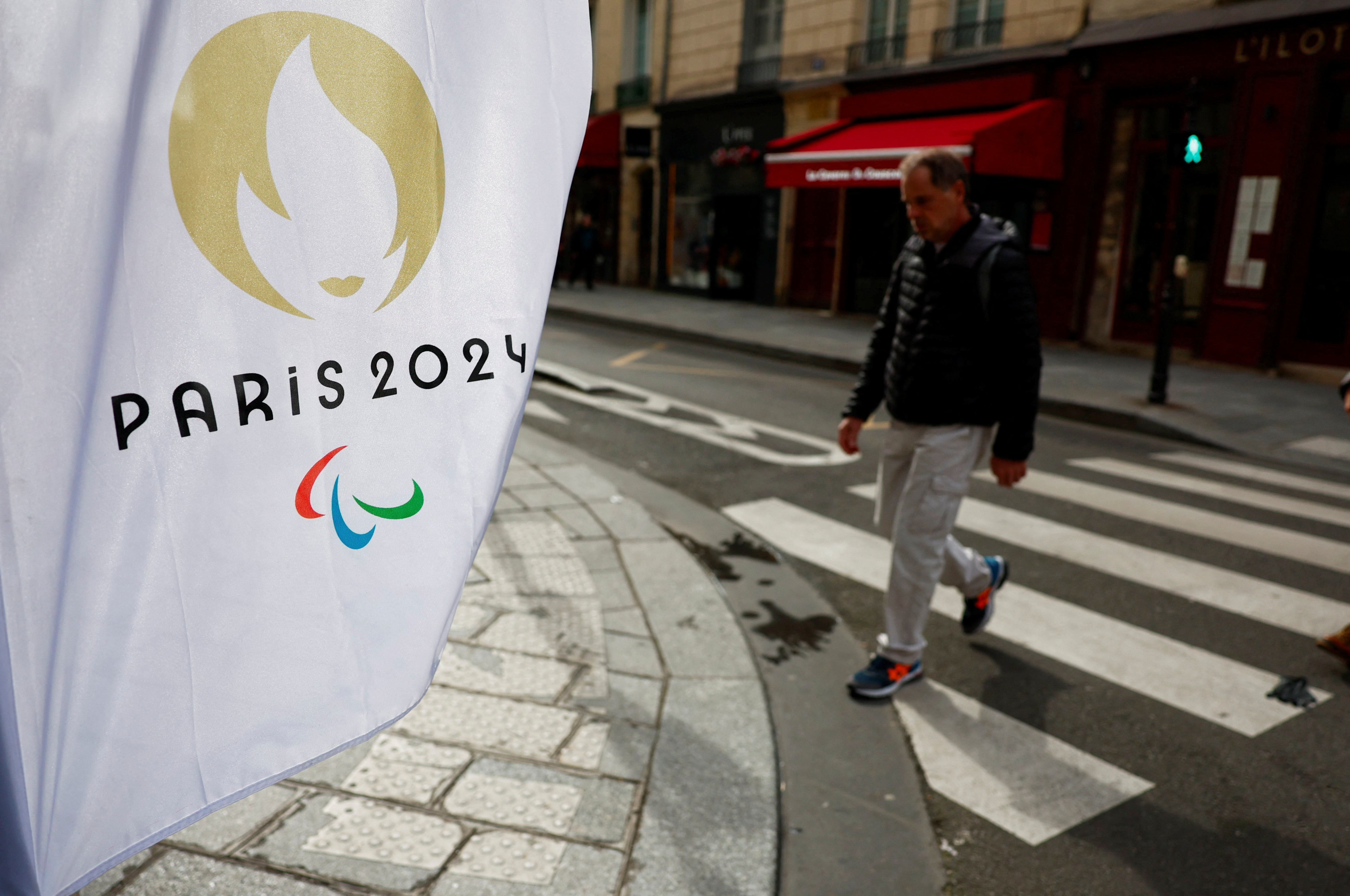 Man walks near a flag with the logo of the Paris 2024 Olympic and Paralympic Games in Paris