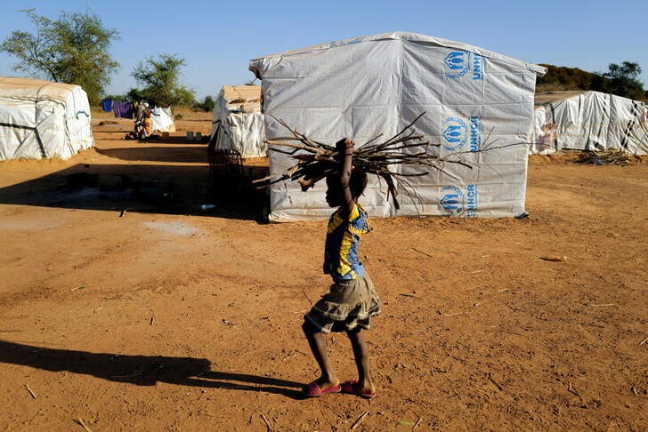 A girl who fled with his parents from attacks of armed militants in the Sahel region carries wood for a cooking fire at a camp for internally displaced people (IDPs) in Kaya