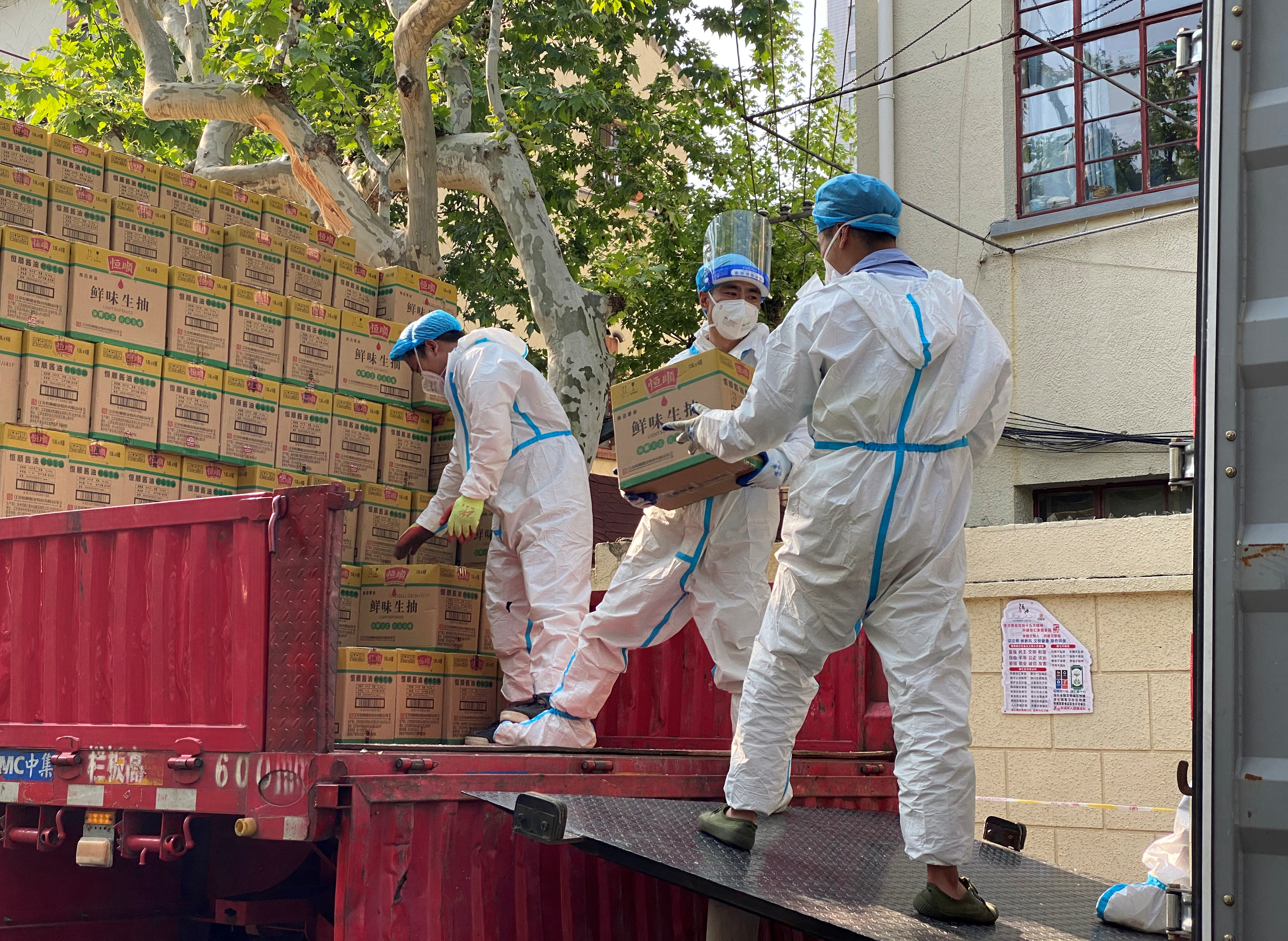 People in protective suits unload boxes labeled soy sauce from a truck, following the coronavirus disease (COVID-19) outbreak in Shanghai