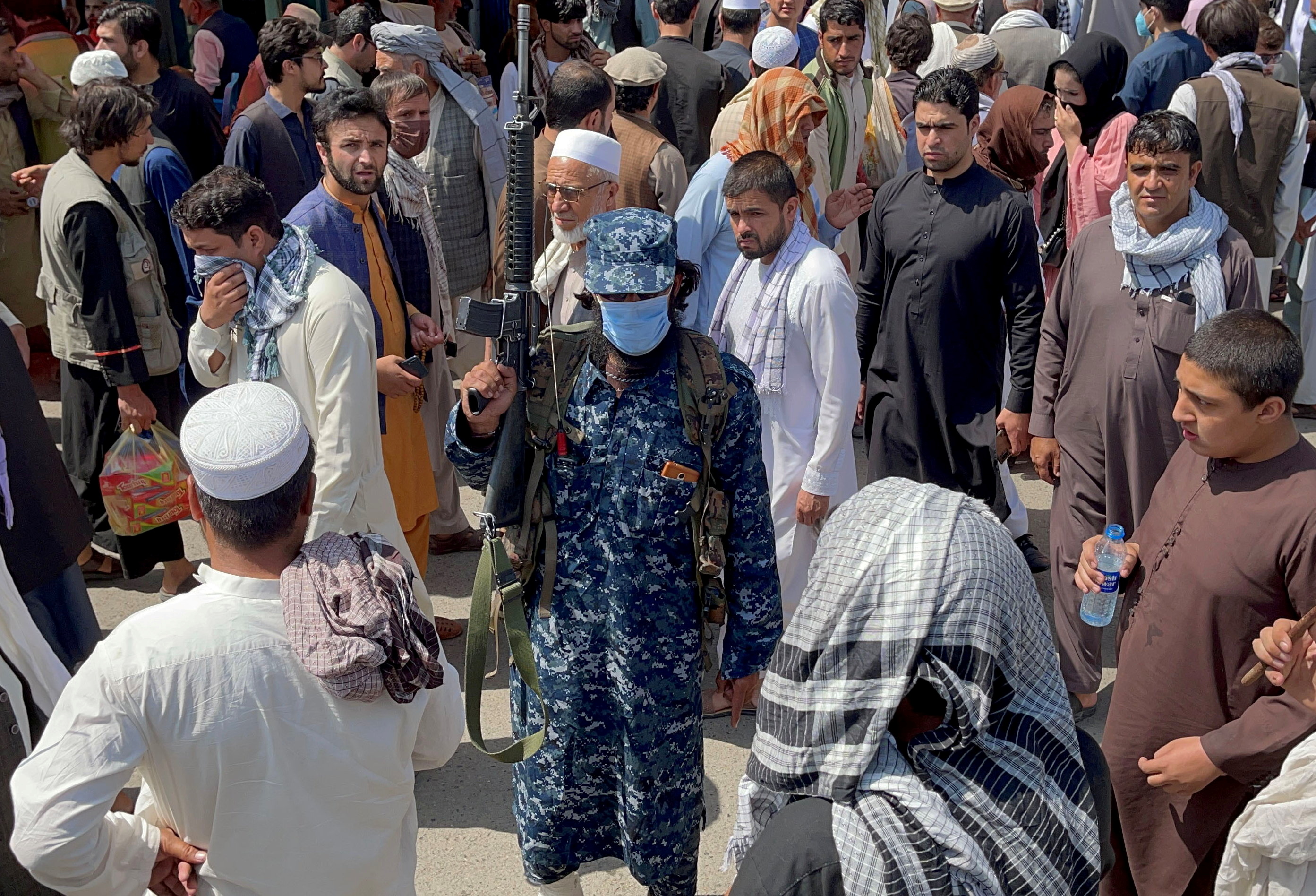 Member of Taliban security forces stands guard among crowds of people in a street in Kabul