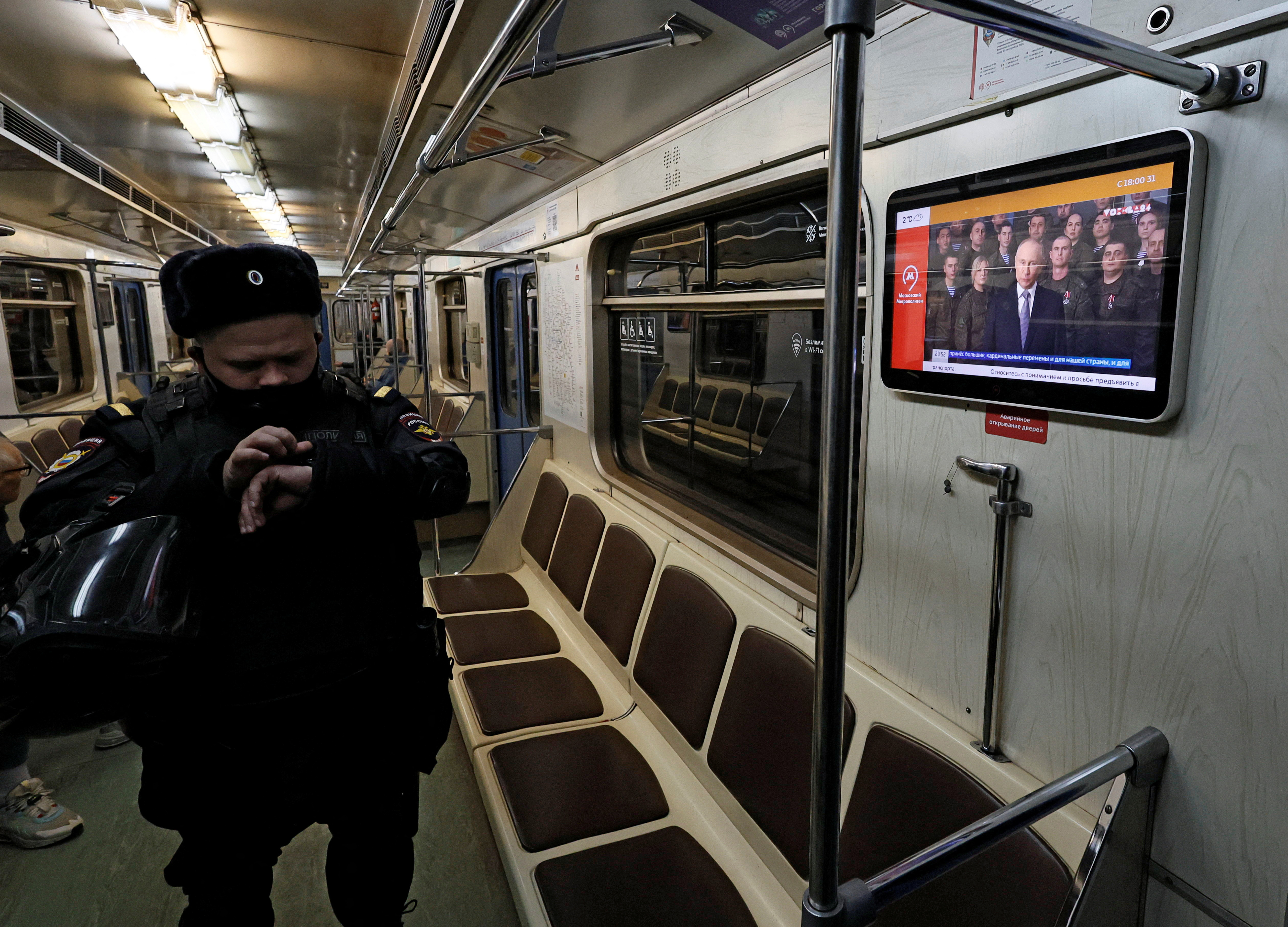 A police officer stands in front of a screen broadcasting Russian President Vladimir Putin's annual New Year address to the nation, in a subway train in Moscow
