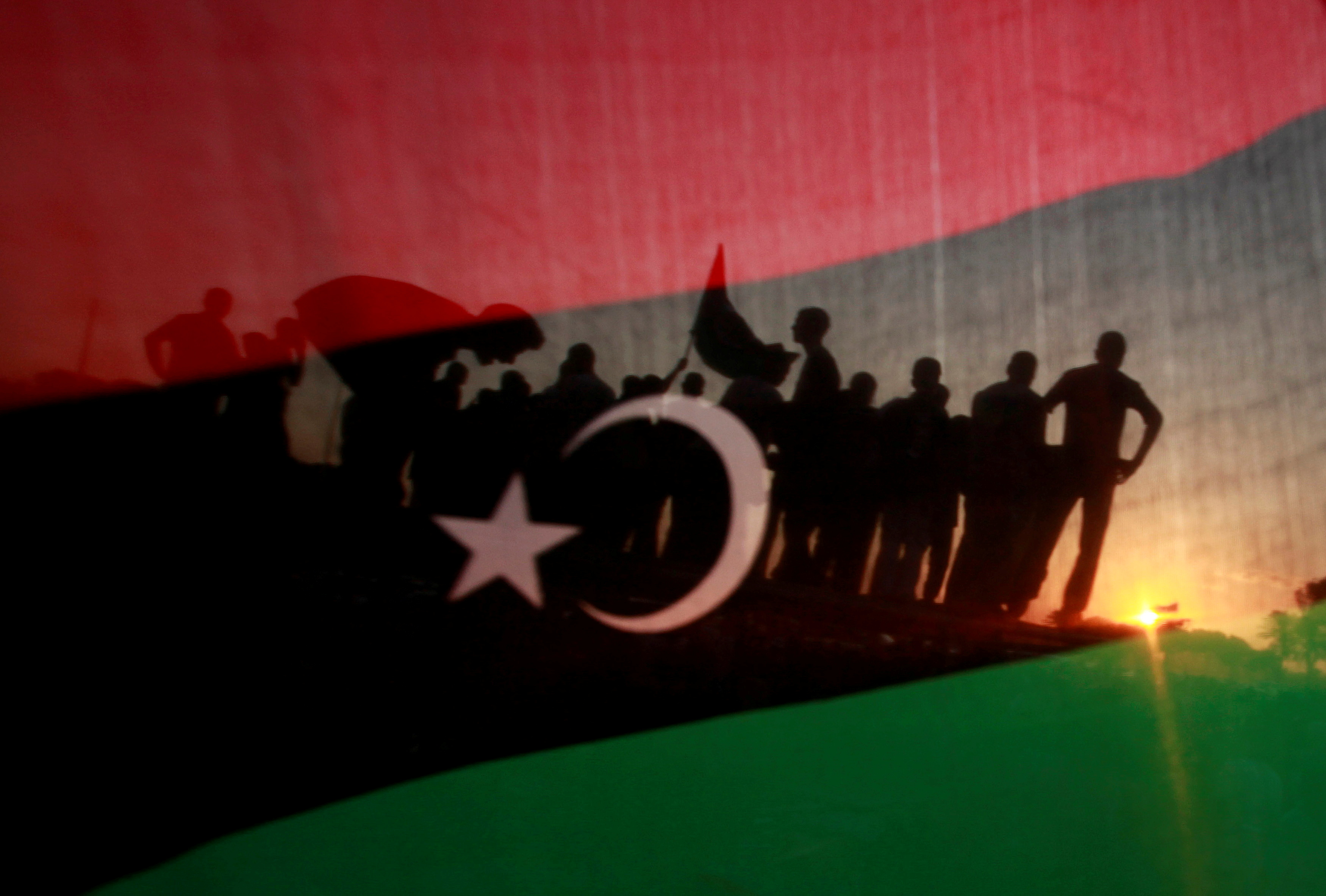 Libyans are seen through a Kingdom of Libya flag during a celebration rally in front of the residence of Muammar Gaddafi at the Bab al-Aziziyah complex in Tripoli