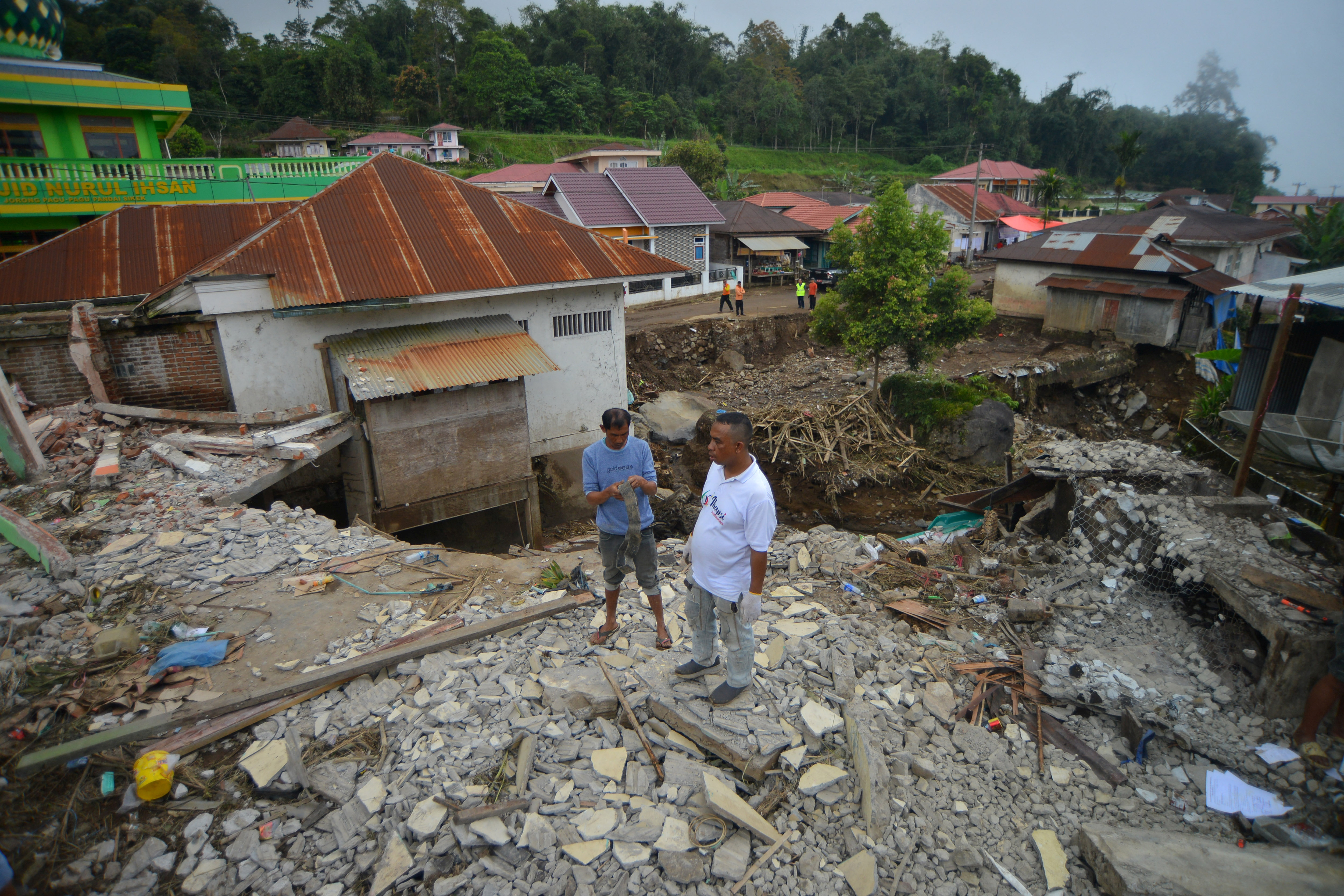 Men stand near a damaged house in an area affected by heavy rain brought flash floods in Tanah Datar