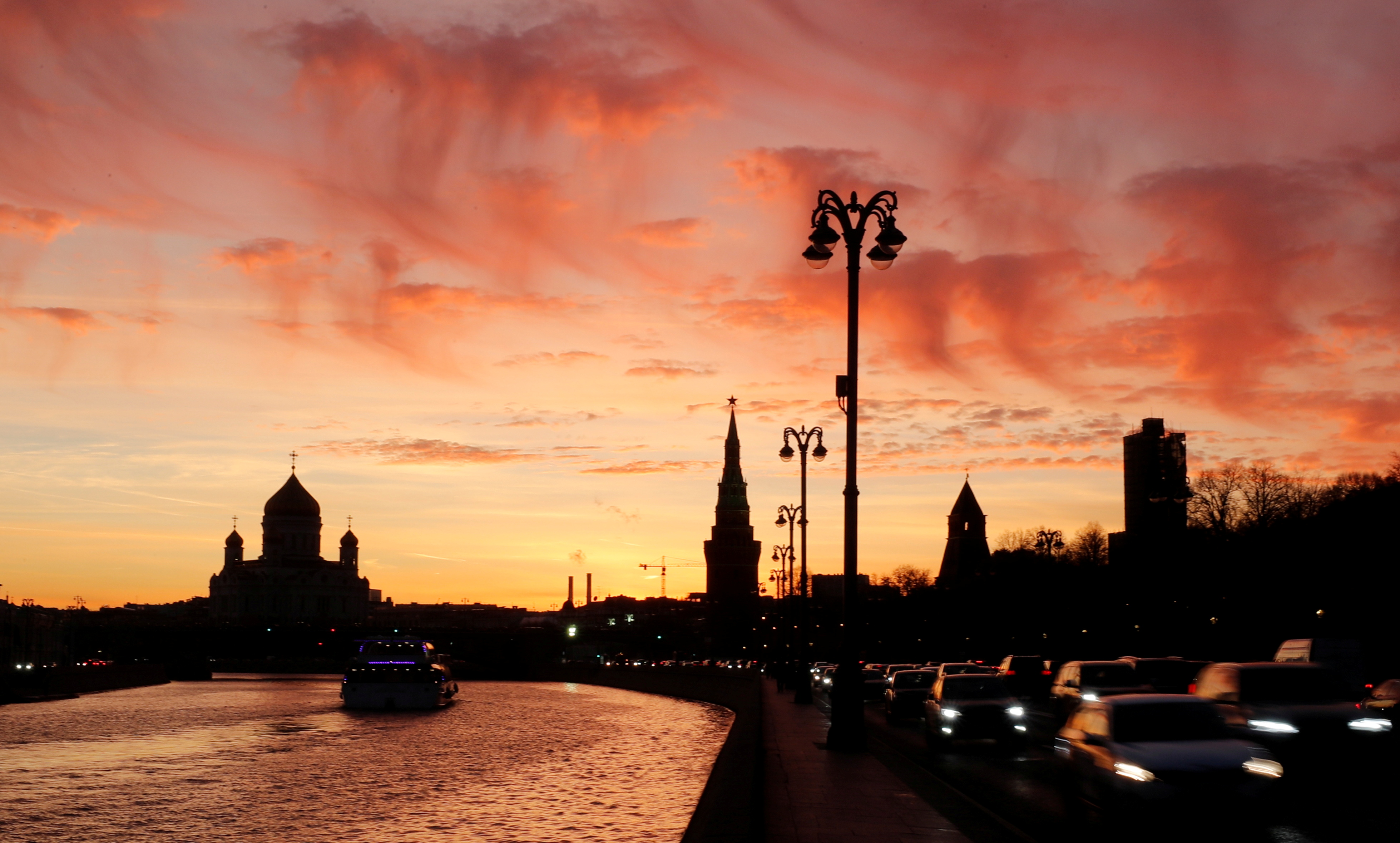 Vehicles travel along the embankment of the Moskva River during sunset in Moscow