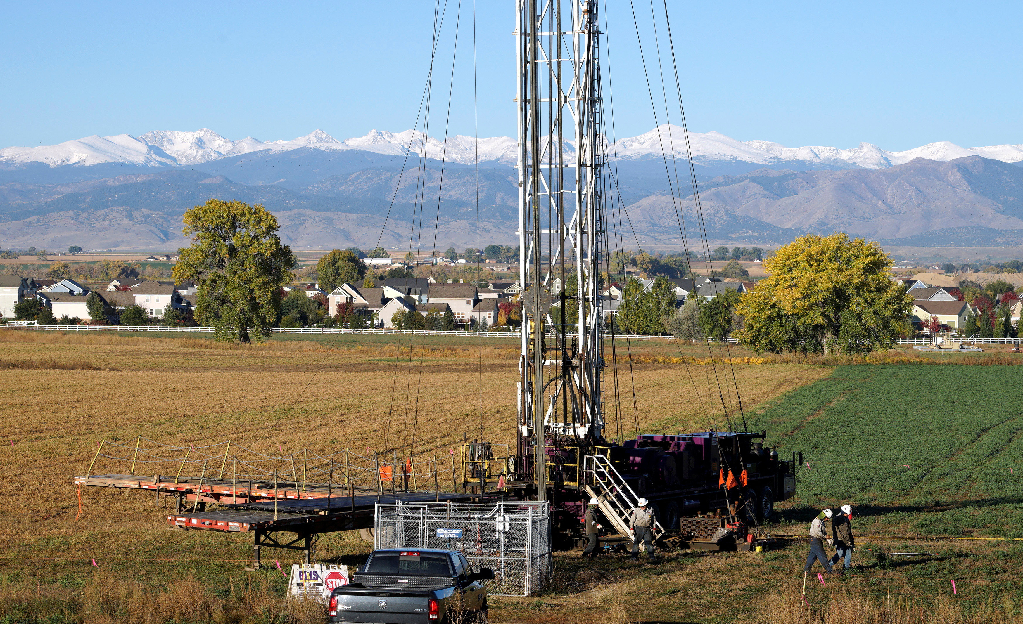 Workers drill a new oil well within sight of houses against a snow-covered Rocky Mountain backdrop near the town of Longmont