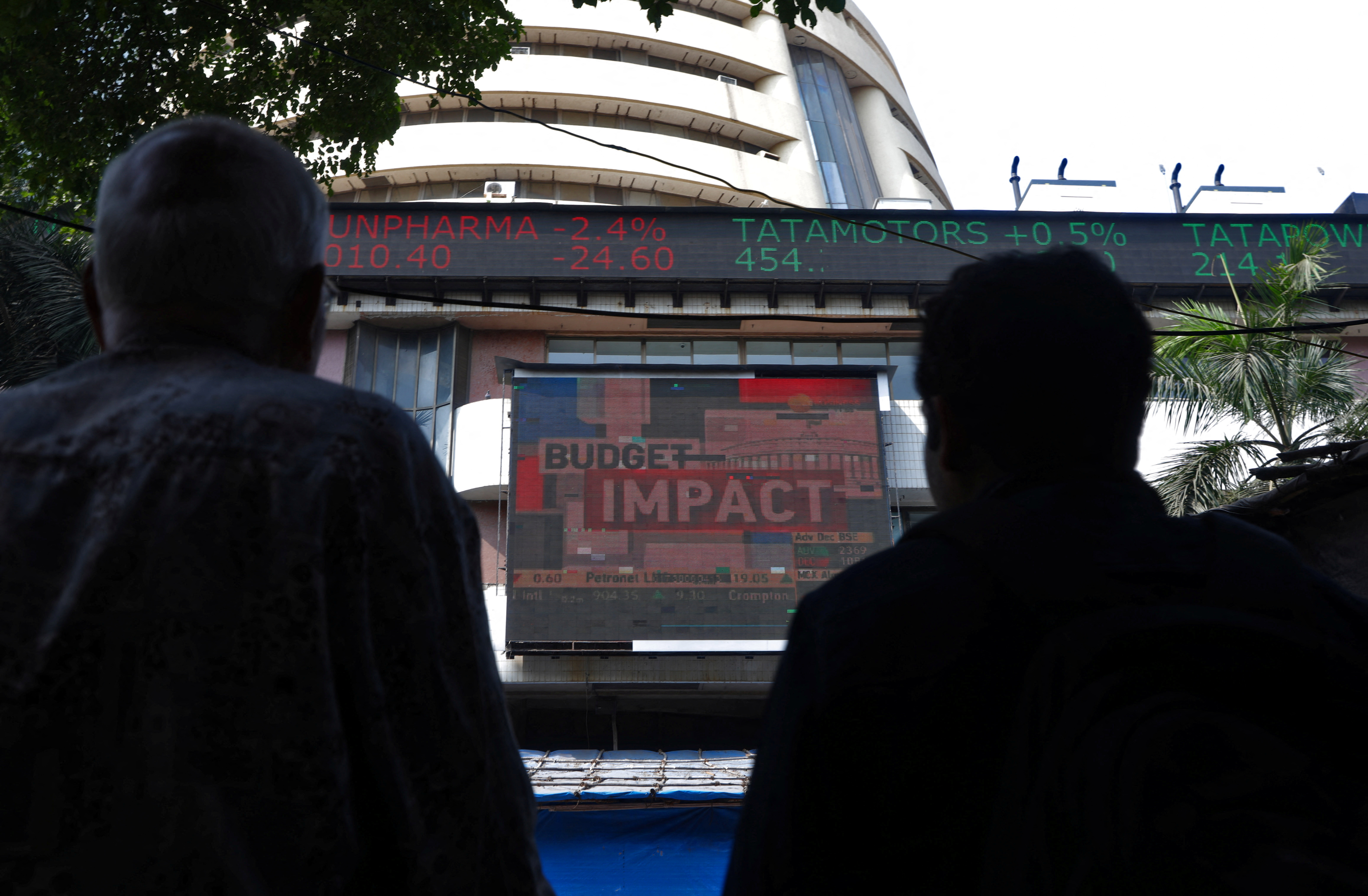 Men watch a screen displaying the Sensex results on the facade of BSE building in Mumbai