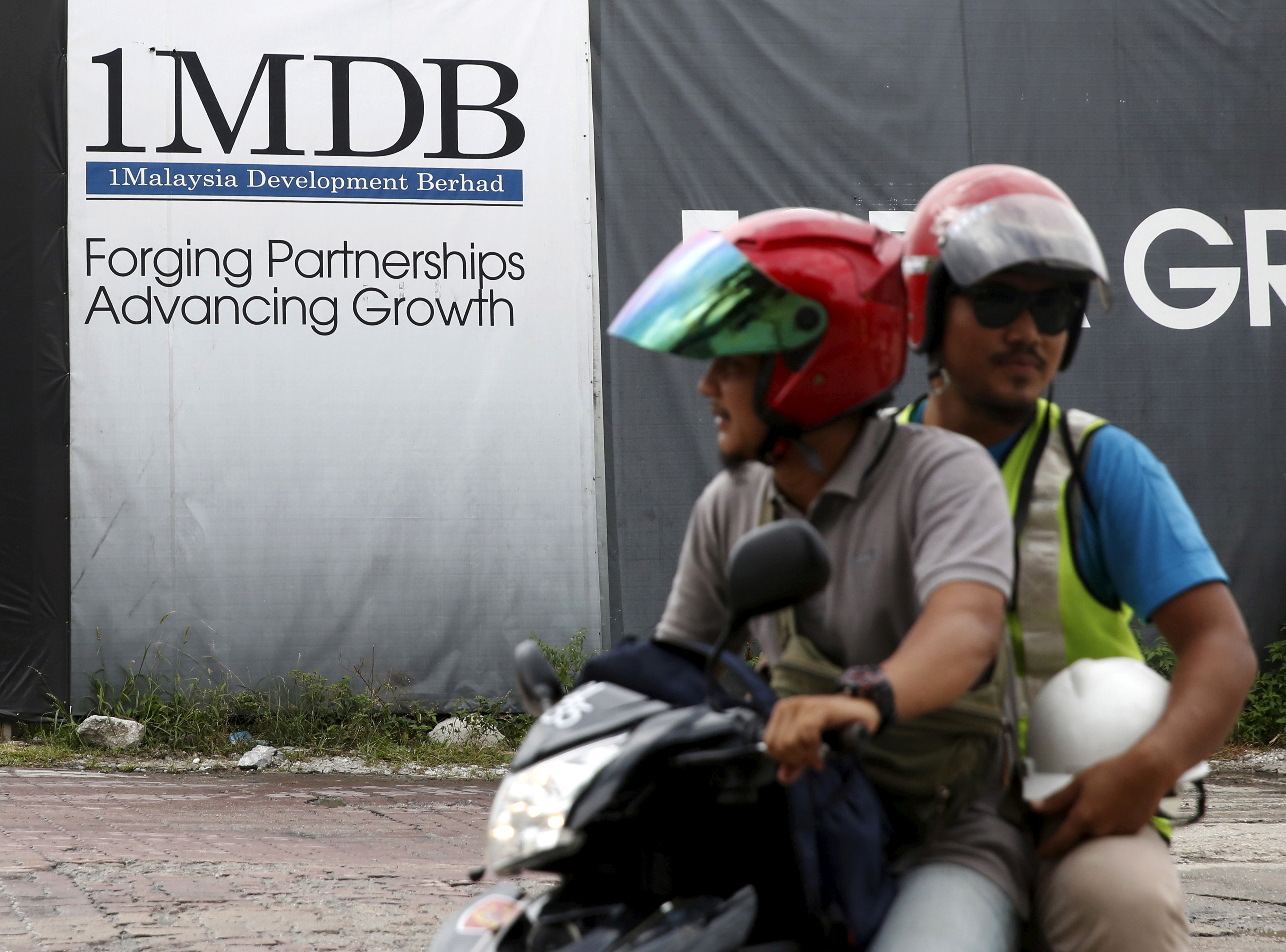 Motorcyclists pass a 1Malaysia Development Berhad (1MDB) billboard at the Tun Razak Exchange development in Kuala Lumpur, Malaysia