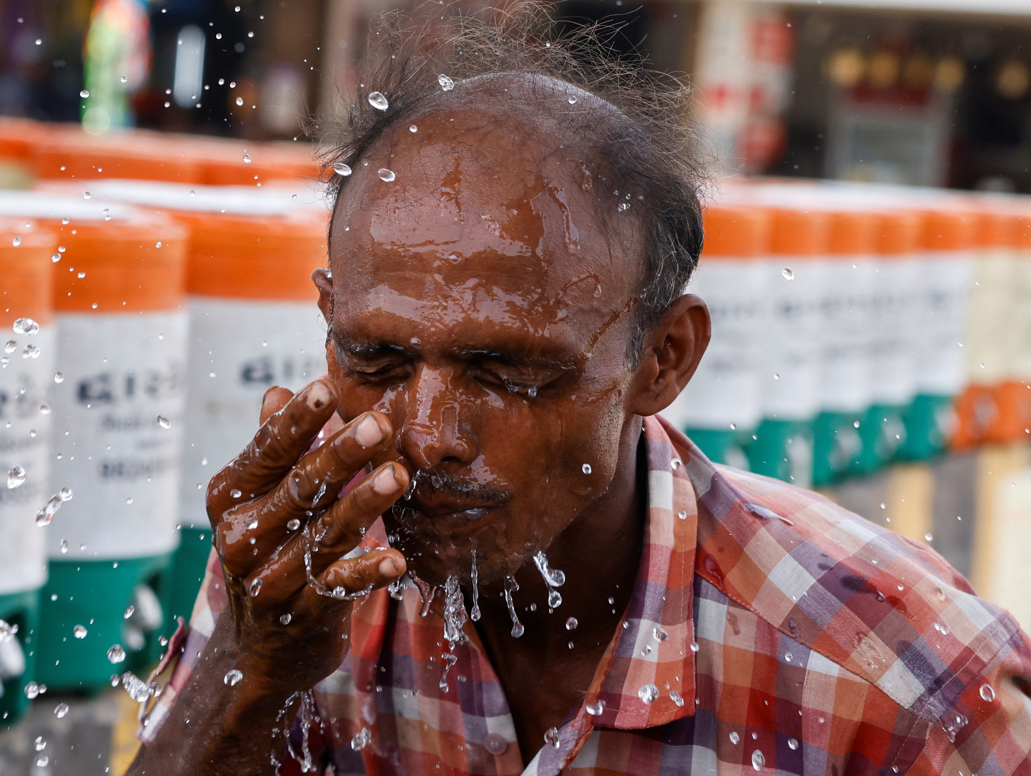 A man sprays cold water on his face from a water jar during a heatwave in Ahmedabad