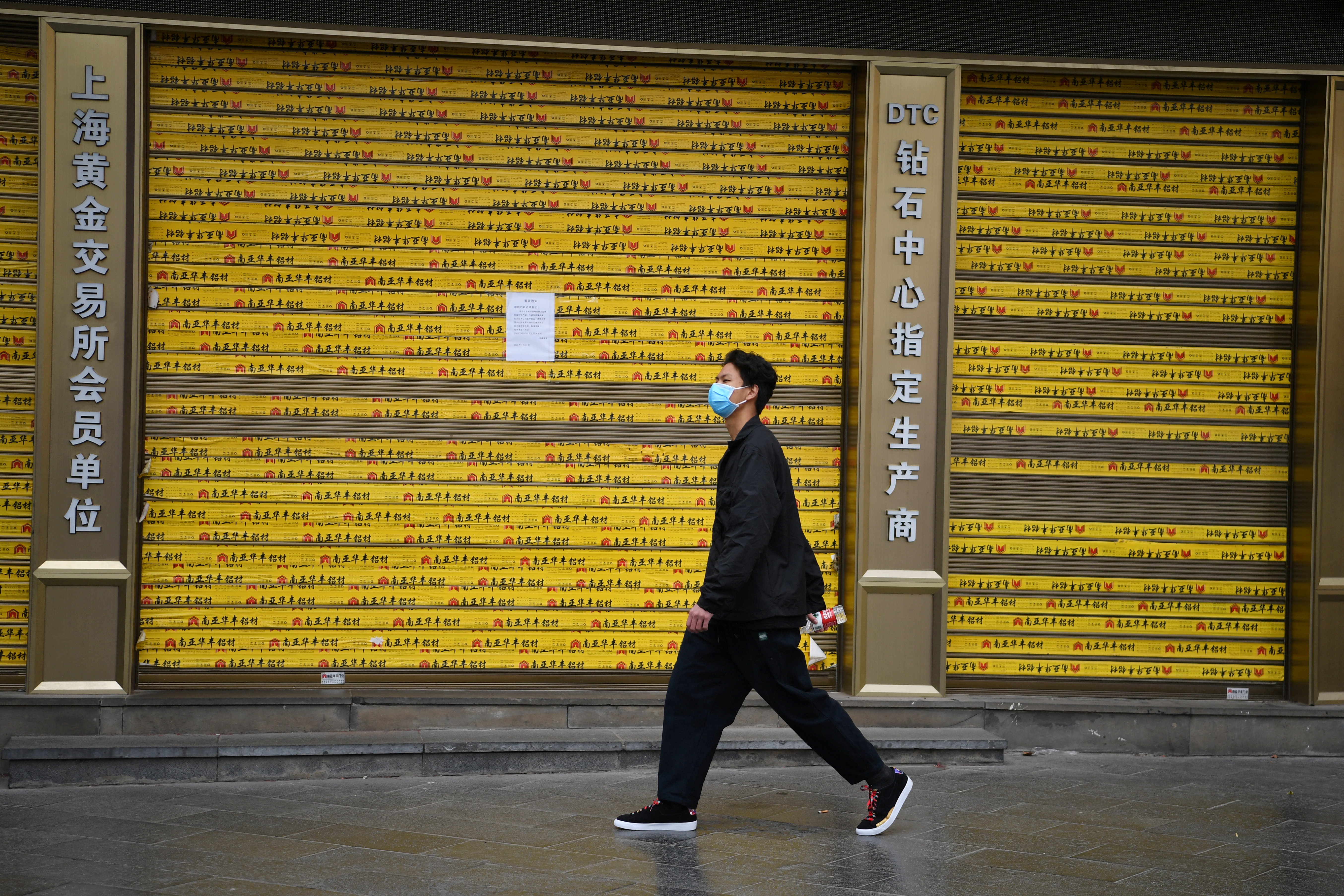 Man wearing a face mask walks past a closed shop with a notice on the outbreak of the new coronavirus, in Kunming
