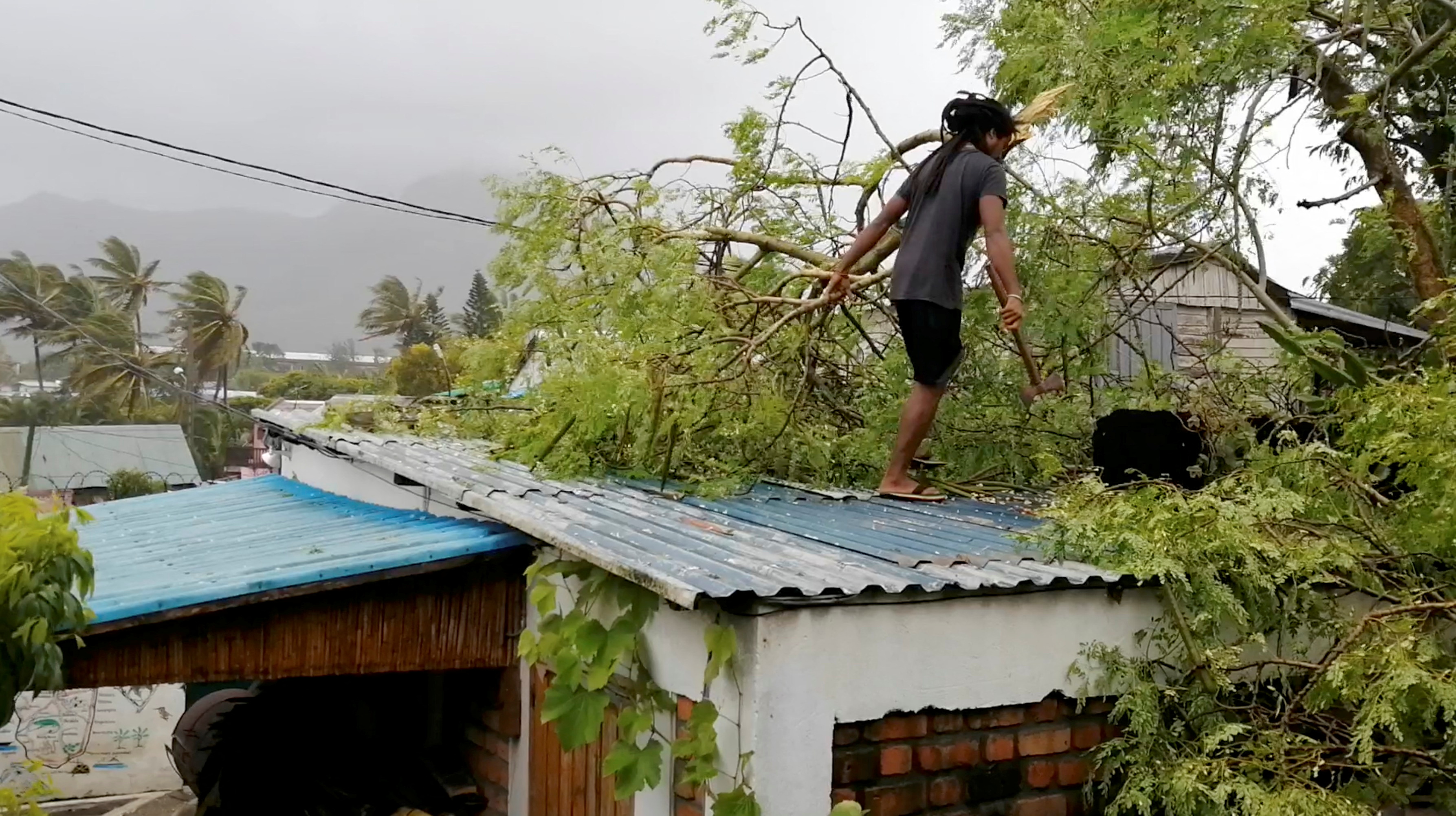 A man removes a fallen branch from the roof of a house, amidst Cyclone Emnati, in Fort Dauphin