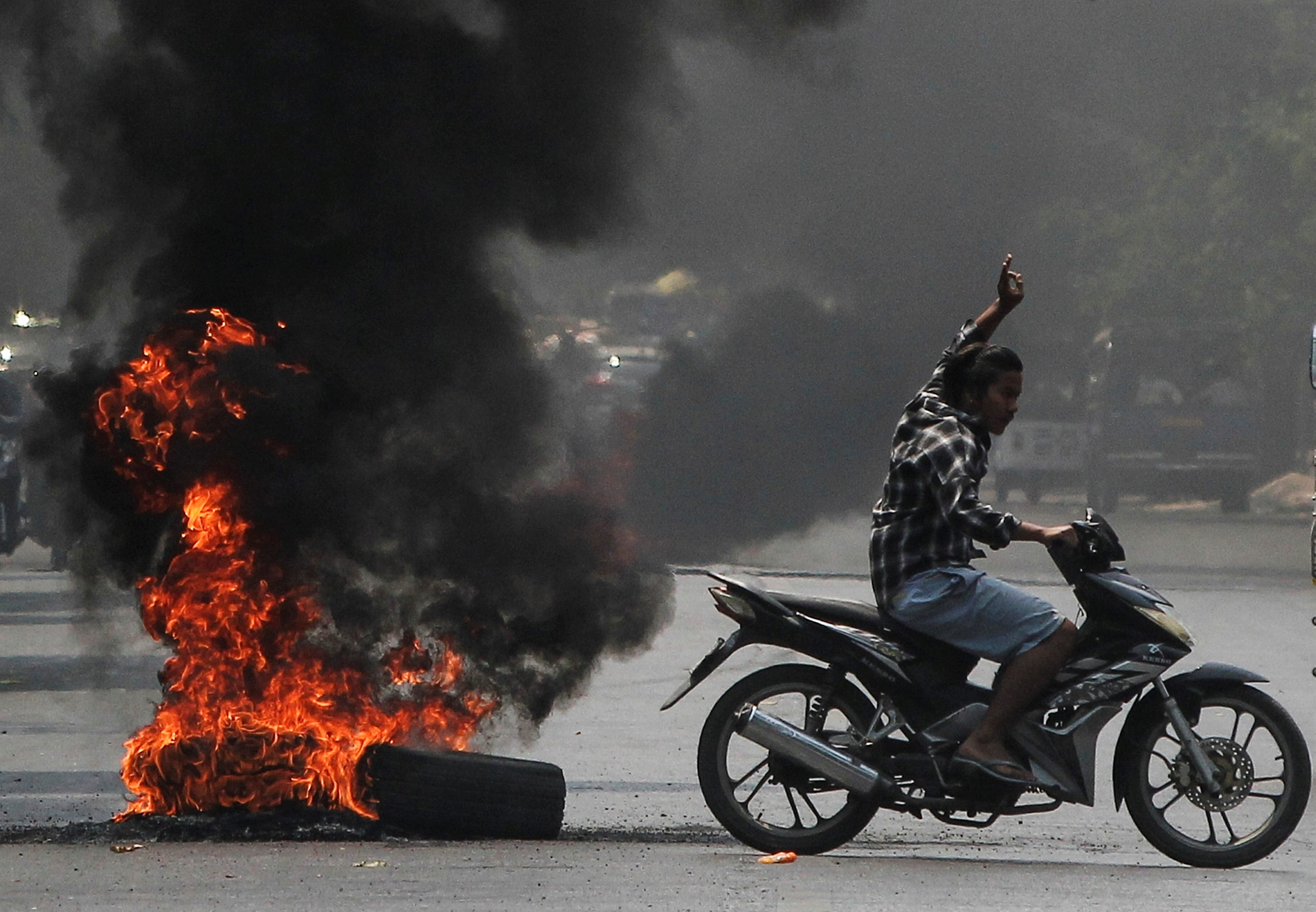 Man flashes three-finger salute next to burning tires during a protest against the military coup, in Mandalay