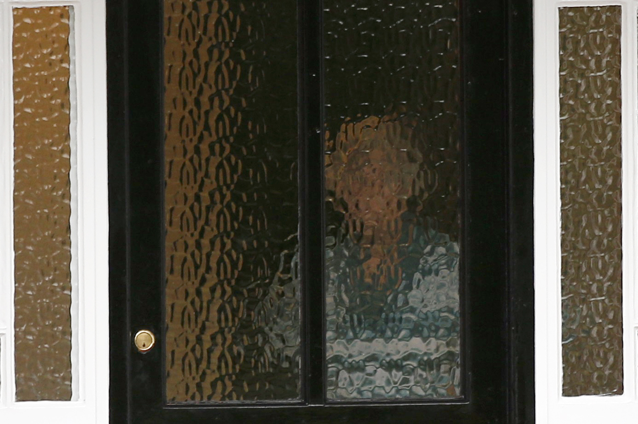 A person stands behind textured glass at an address which has been linked by local media to former British intelligence officer Christopher Steele, who has been named as the author of an intelligence dossier on President-elect Donald Trump, in Wokingham