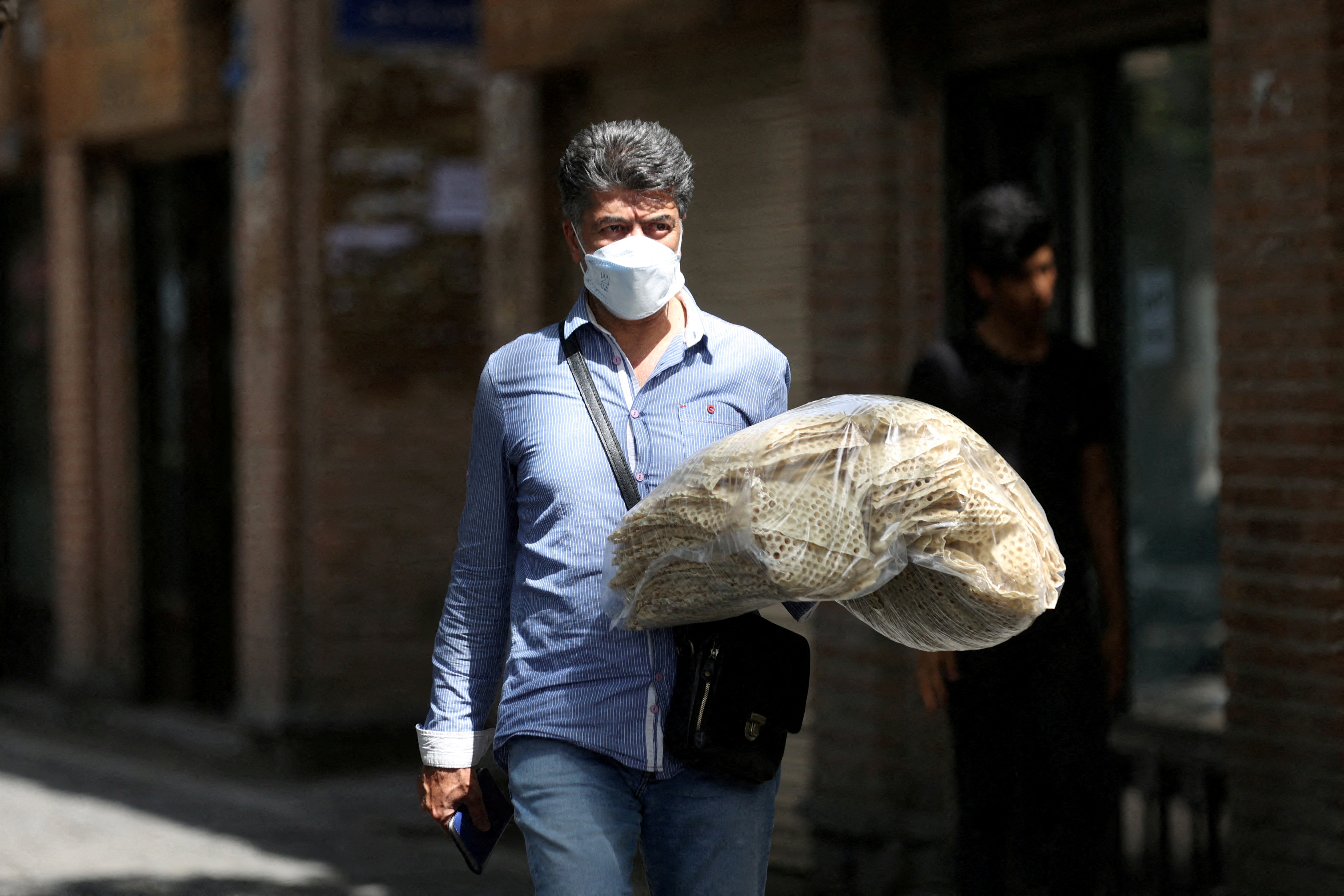 An Iranian man holds stacks of bread as he walks along a street in Tehran