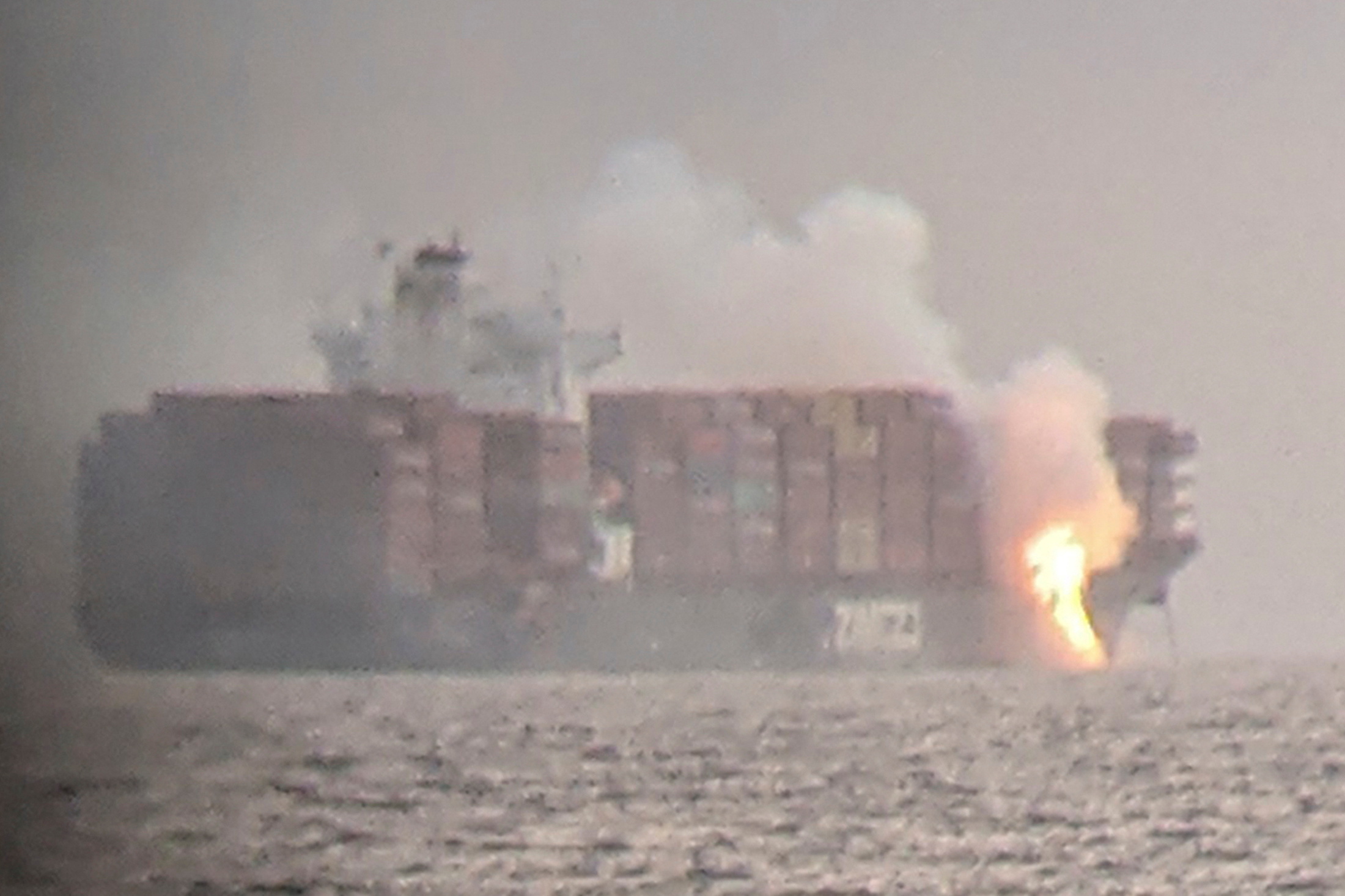 Fire cascades down from the deck of the container ship ZIM Kingston into the waters off the coast of Victoria, British Columbia, Canada, October 23, 2021, as seen through a pair of binoculars, in this image obtained via social media. SURFRIDER FOUNDATION CANADA via REUTERS 