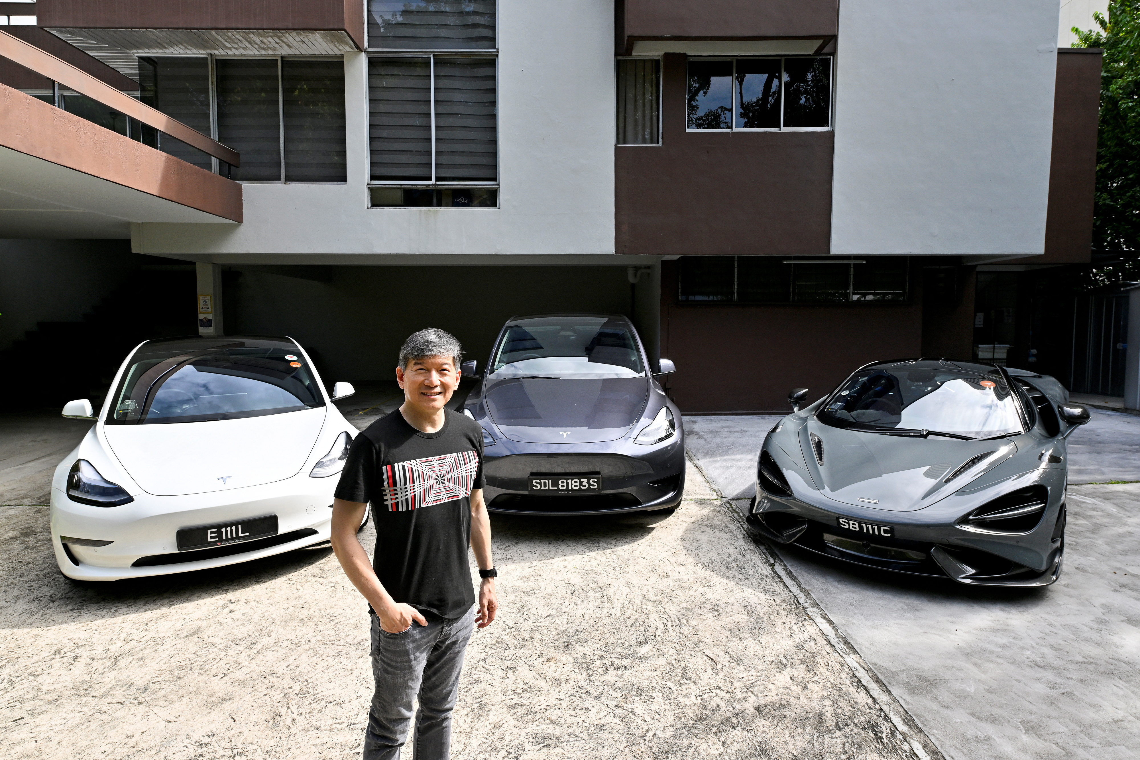 Eu Gene Goh poses for a picture with his three cars, a Tesla Model 3, a Tesla Model Y and a McLaren 765LT in Singapore