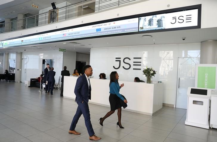 Visitors walk past a reception with an electronic board displaying movements in major indices at the Johannesburg Stock Exchange building in Sandton, Johannesburg