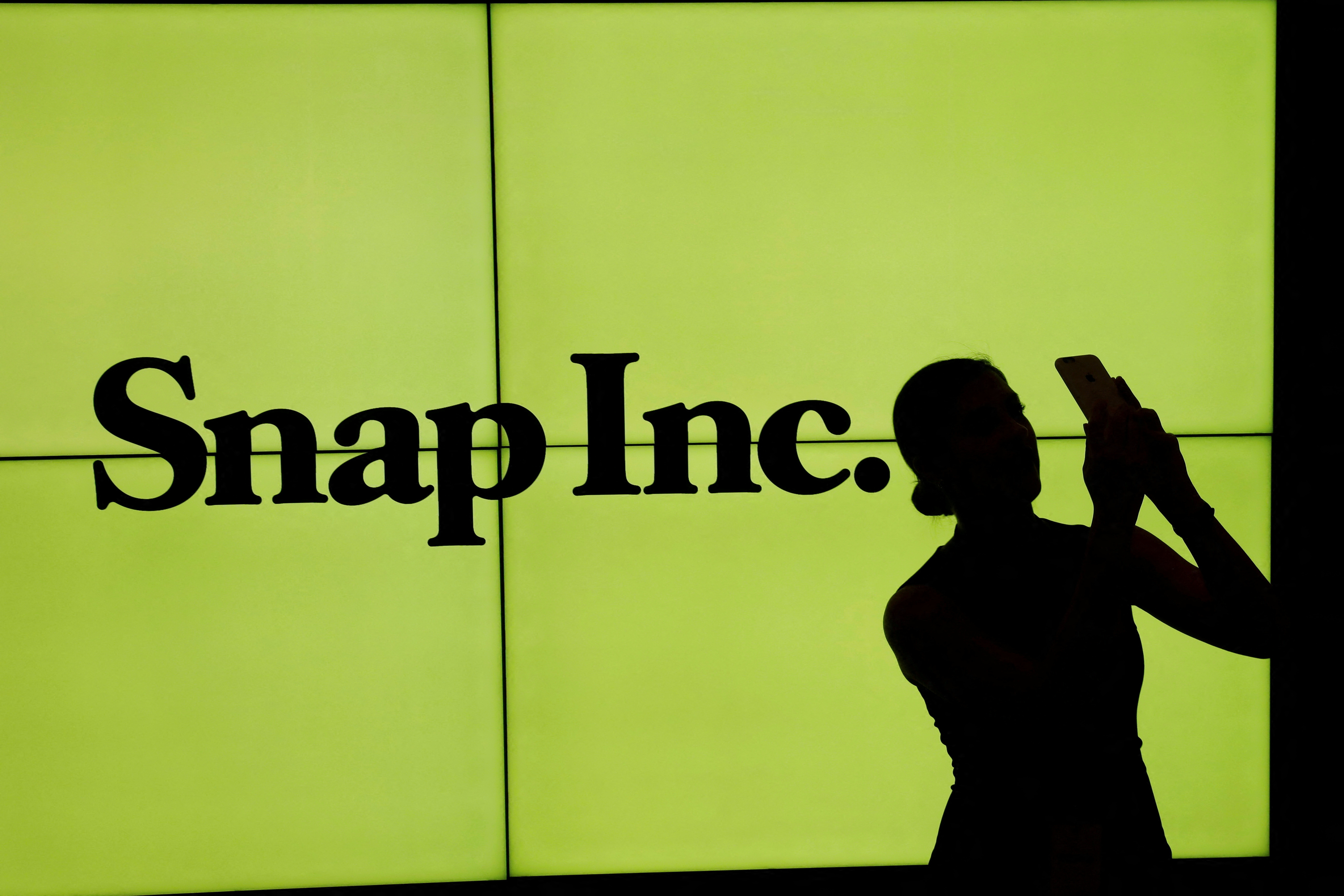 A woman stands in front of the logo of Snap Inc on the floor of the New York Stock Exchange (NYSE) in New York City