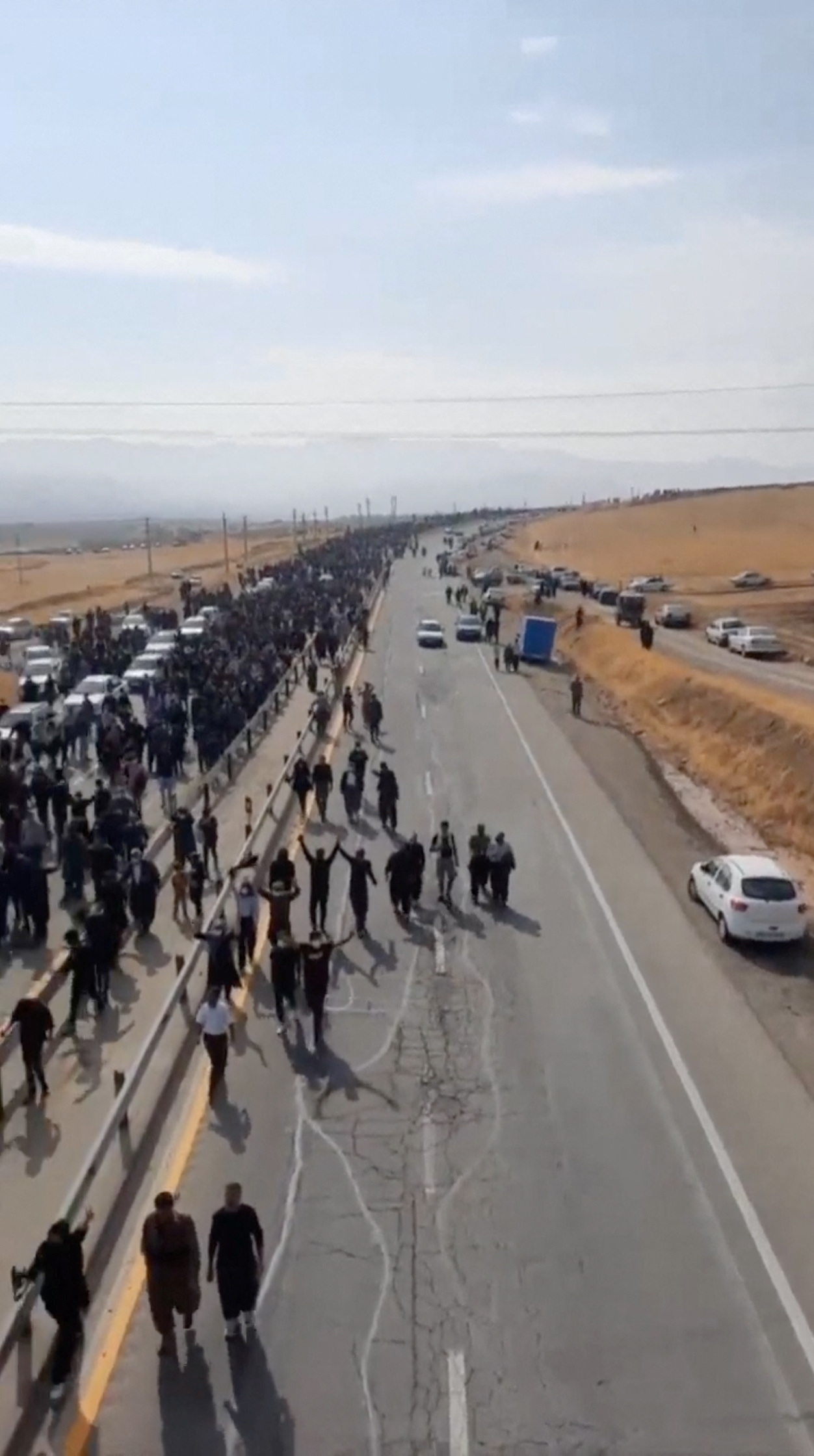 People march down the highway toward the Aychi Cemetery where Mahsa Amini is buried, near Saqez