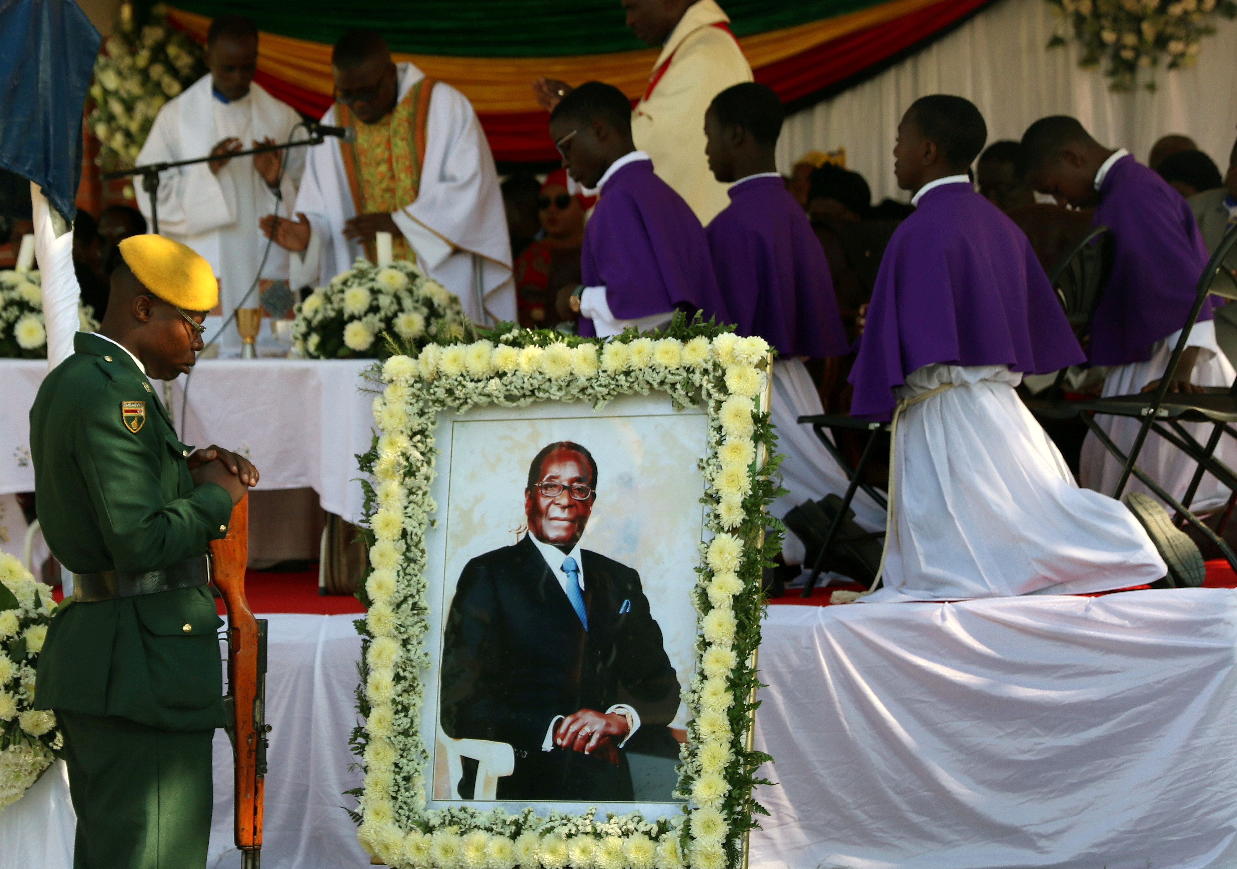 Soldiers stand beside a picture of former Zimbabwean President Robert Mugabe during a church service before his burial at his rural village in Kutama