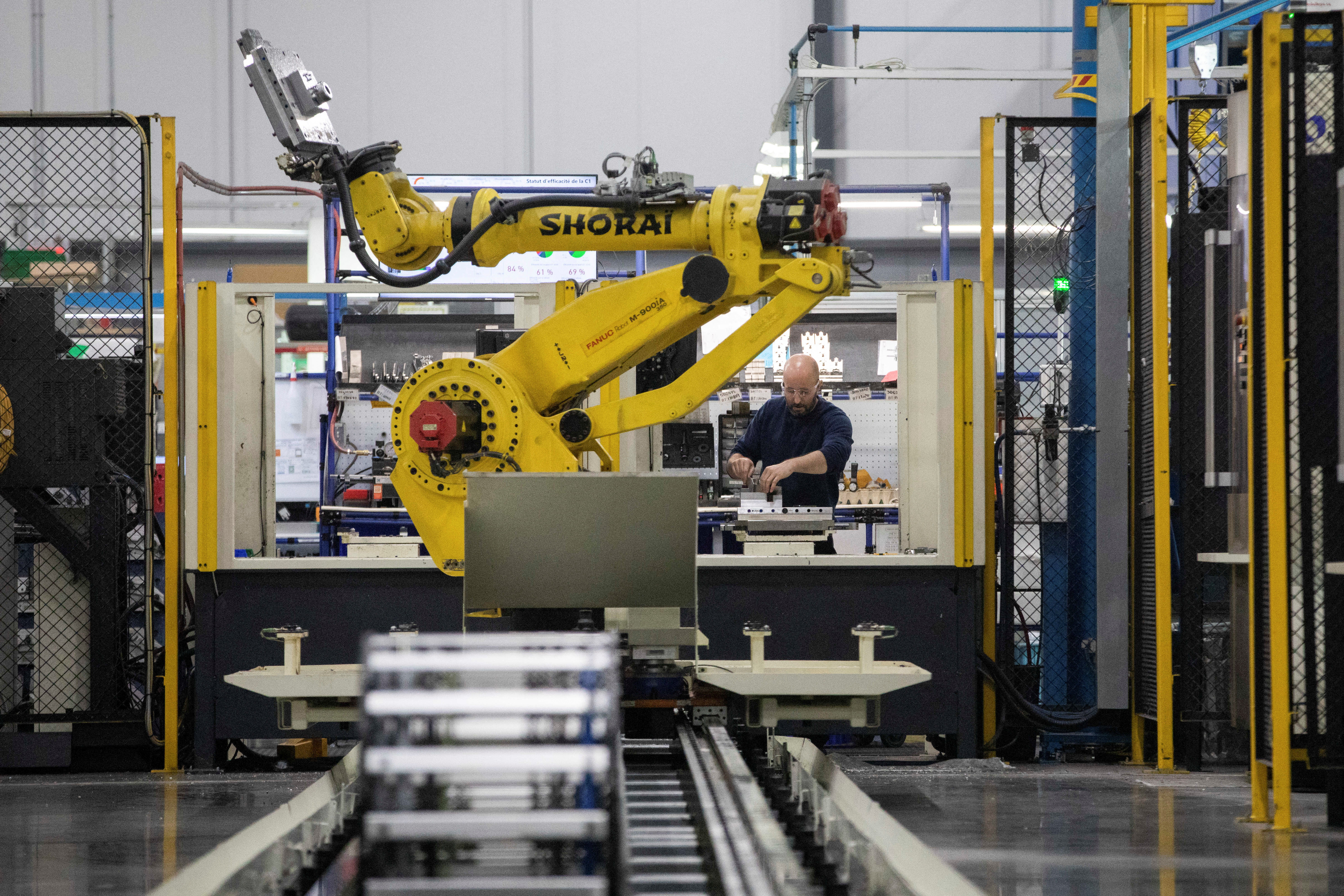 A factory worker works on an aircraft part, as the robot arm of an automated five-axis cell operates autonomously nearby, at Abipa Canada, in Boisbriand