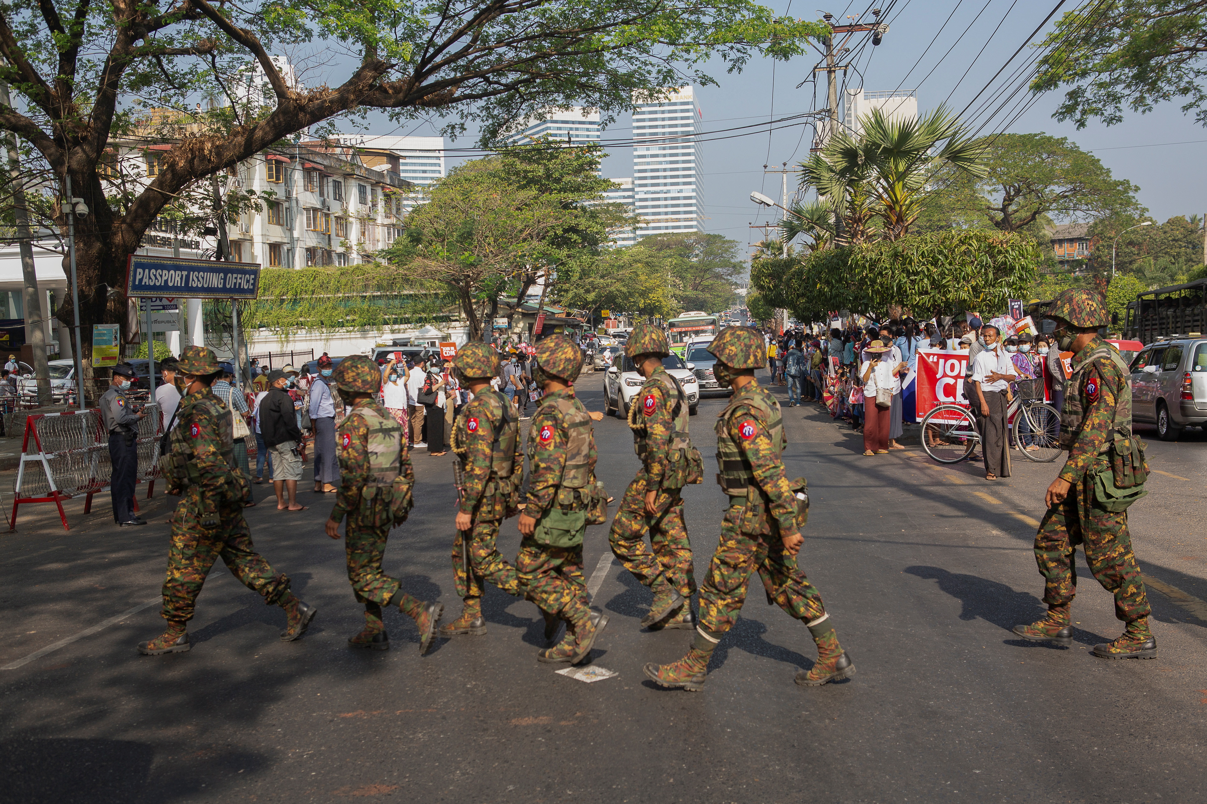 Soldiers cross a street as people gather to protest against the military coup, in Yangon
