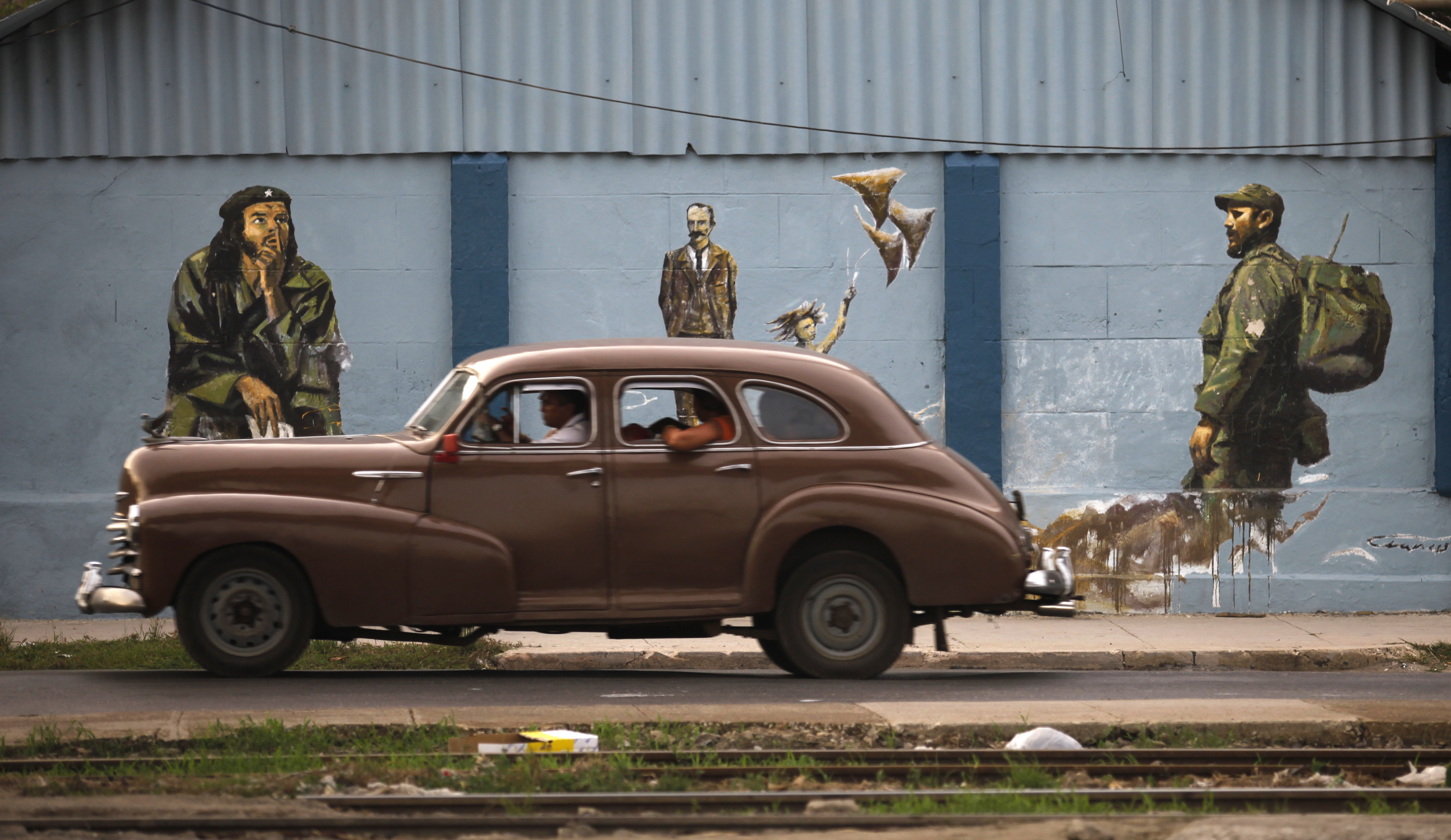A vintage car drives by a mural showing Cuba's former leader Fidel Castro in Havana