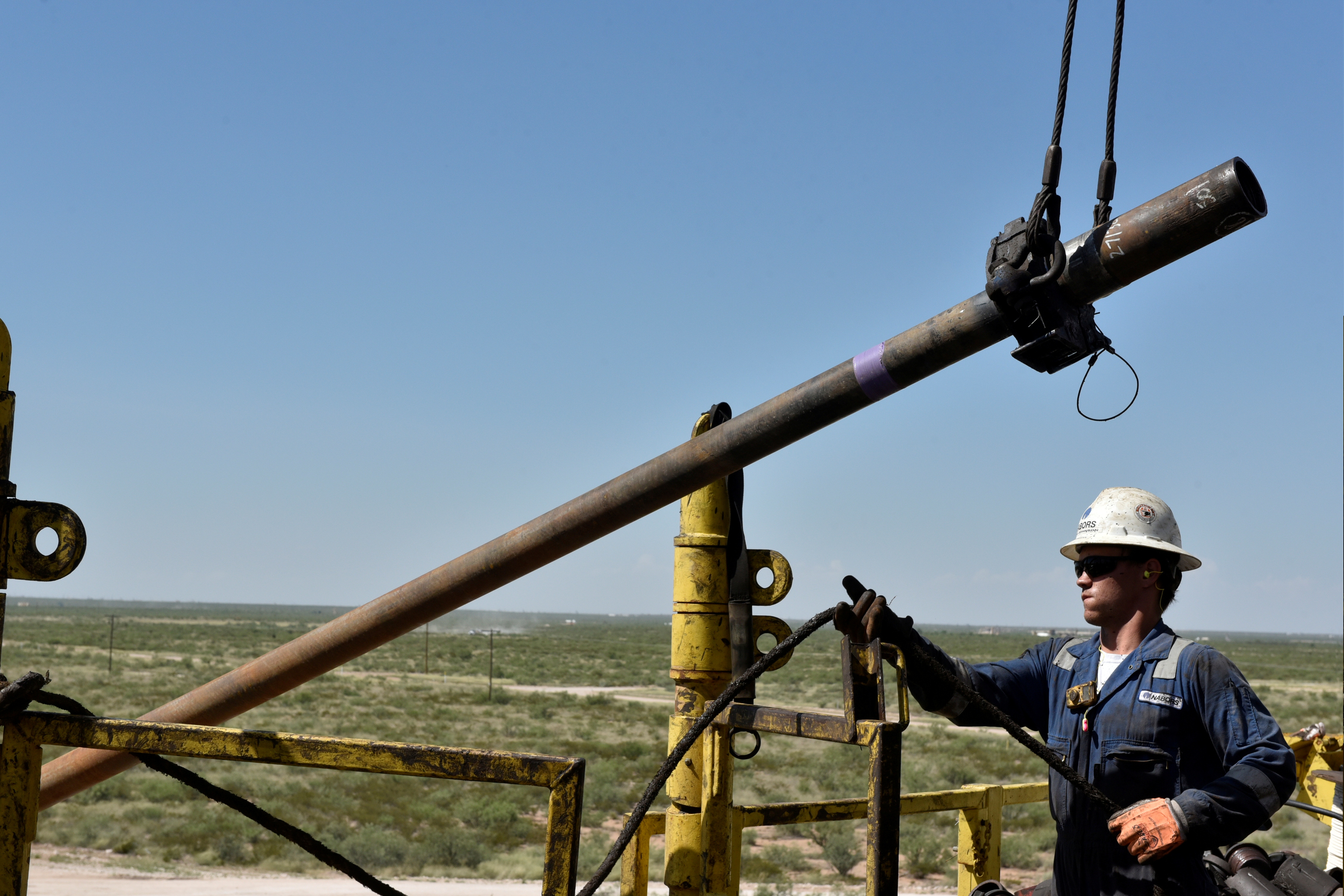 A drilling crew member raises drill pipe onto the drilling rig floor on an oil rig in the Permian Basin near Wink