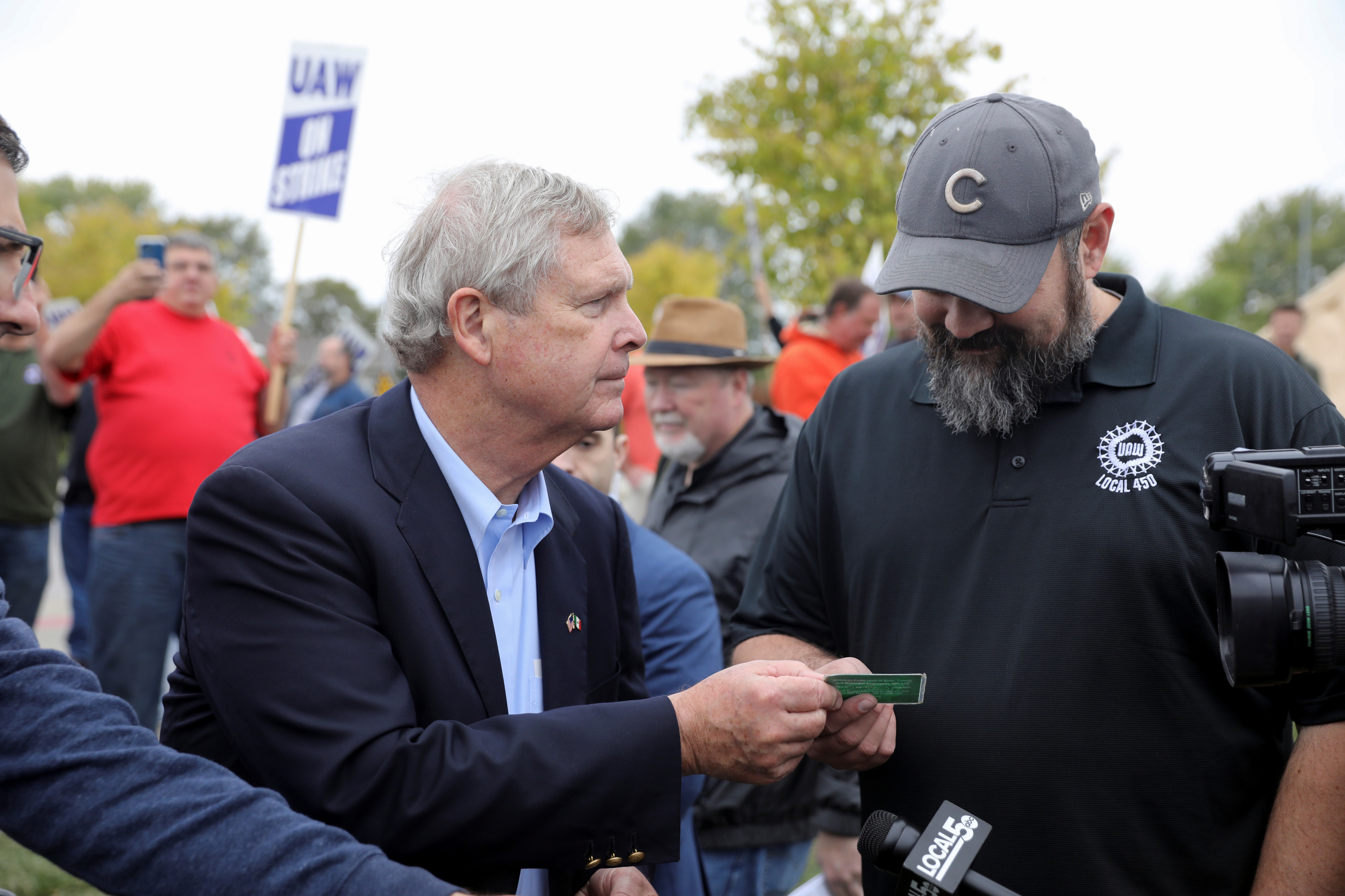 U.S. Agriculture Secretary Tom Vilsack shows his union membership card to Justin Limke as he visits striking members of the United Auto Workers (UAW) at the Deere & Co farm equipment plant in Ankeny, Iowa