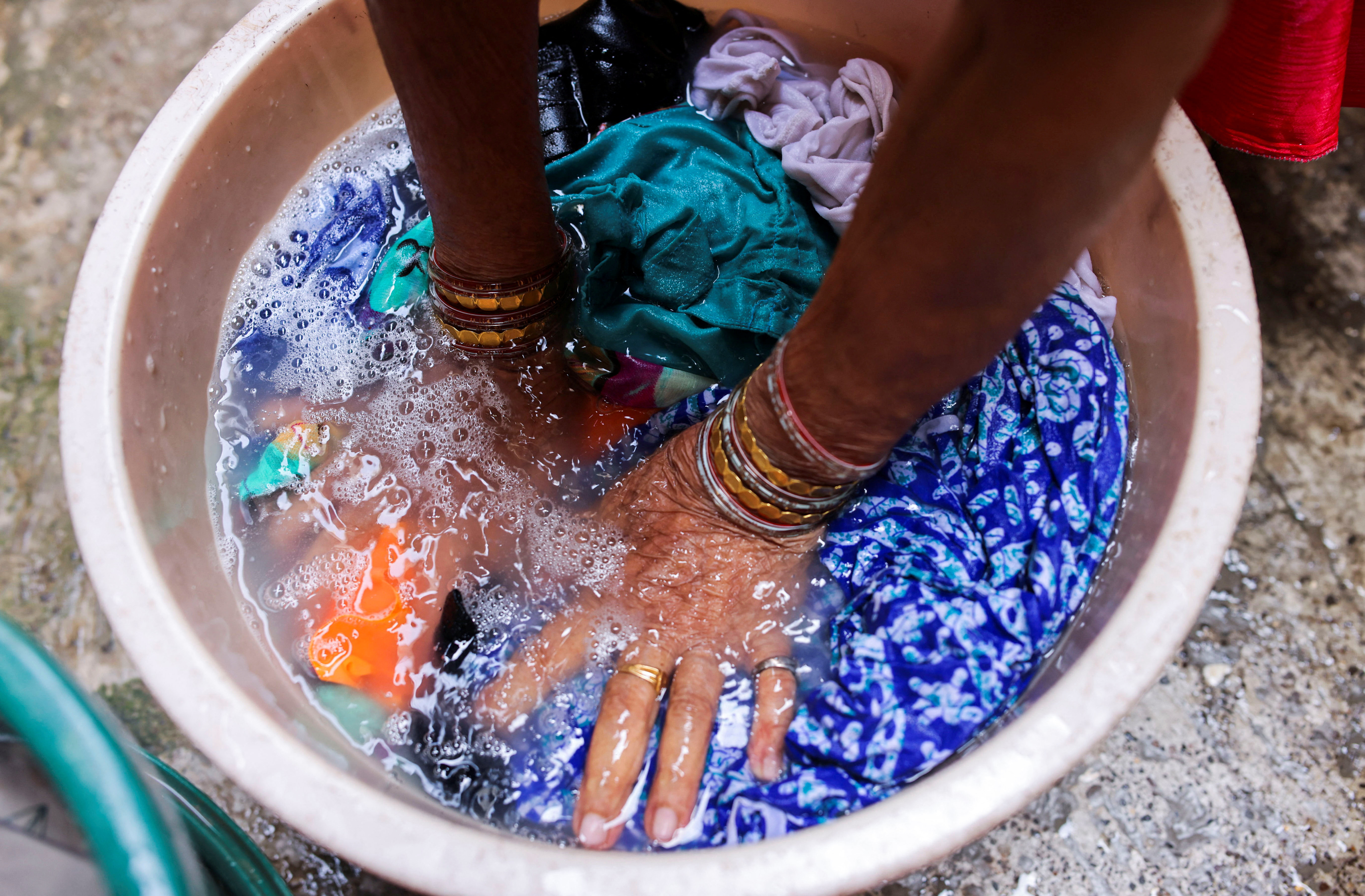 A woman washes clothes with a plastic sachet portion of Unilever's Surf Excel laundry detergent outside her house in Mumbai