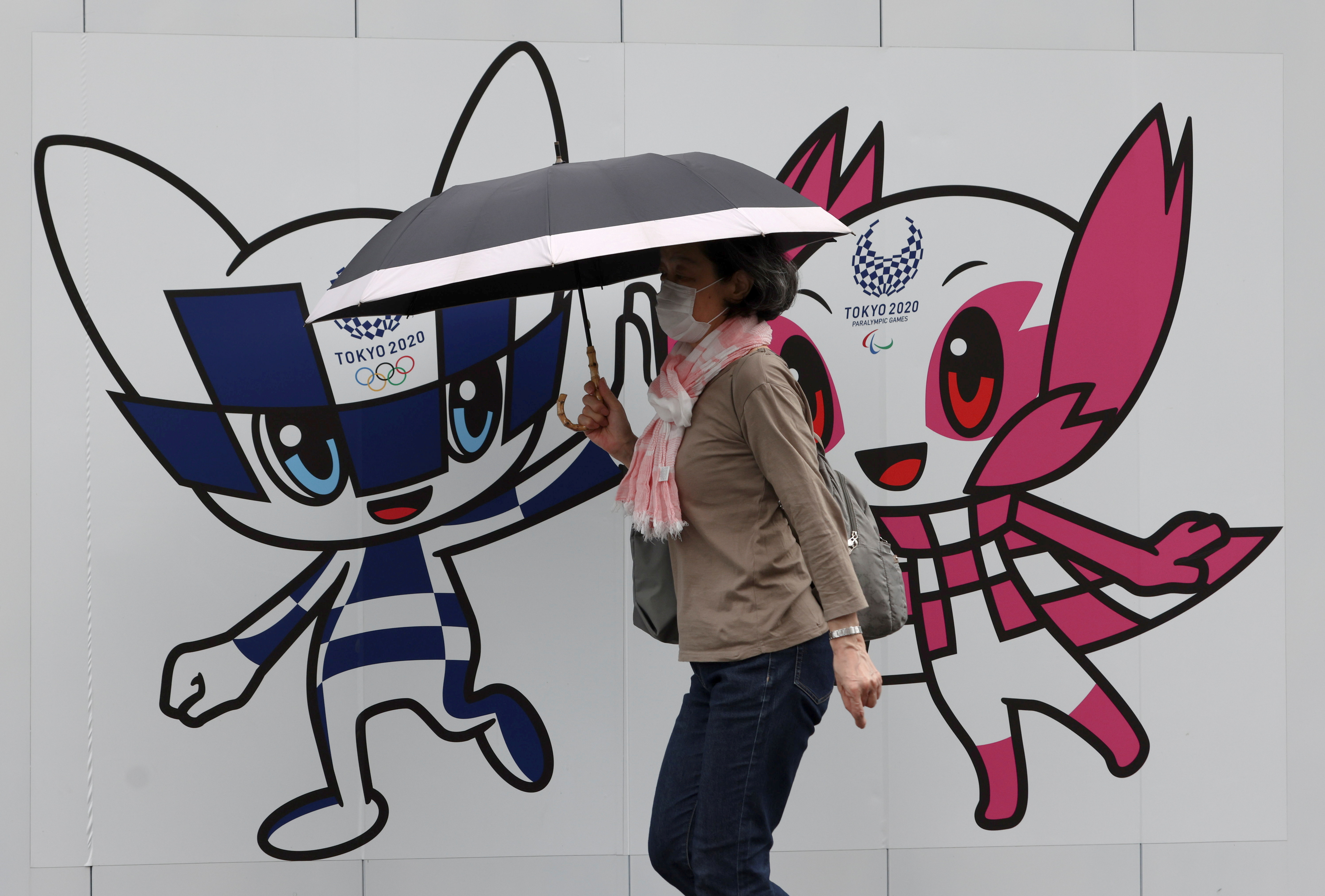A woman wearing a protective face mask walks in front of a wall decoration featuring Tokyo 2020 Olympic Games mascot Miraitowa and Paralympics mascot Someity in Tokyo
