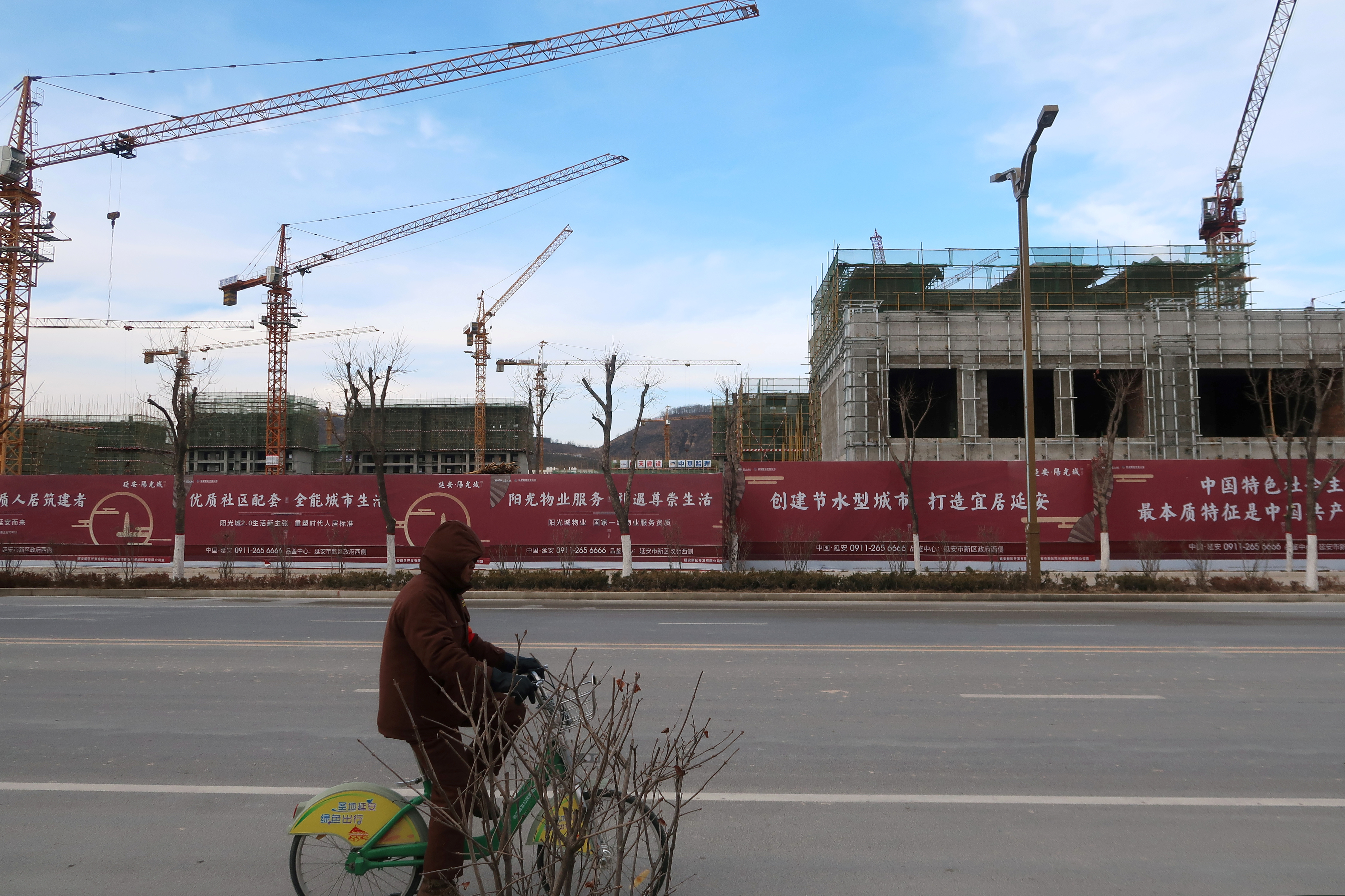 Man rides a bicycle past a Yango Group real estate project under construction in Yanan New Zone