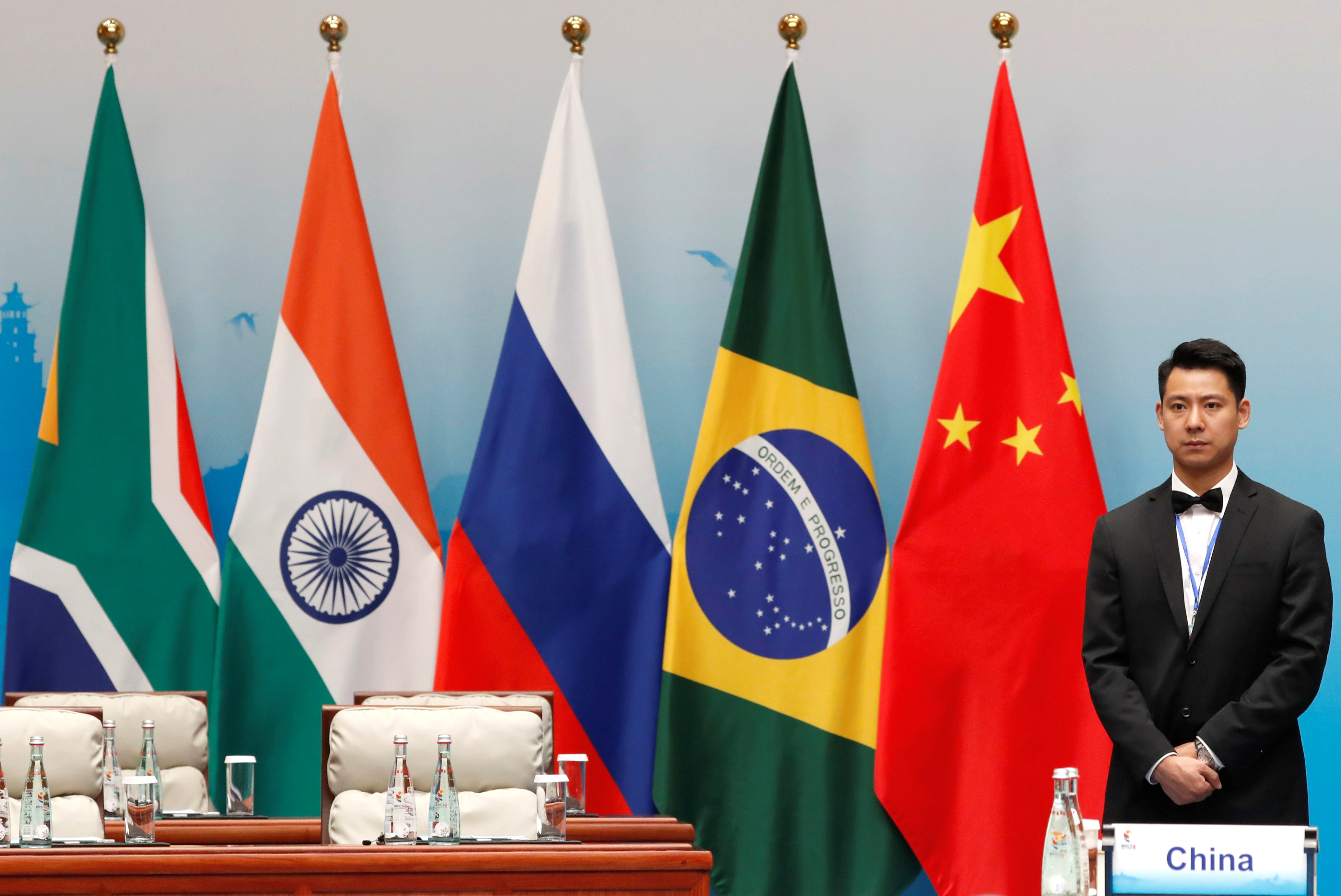 Un participant stă lângă steaguri ale Africii de Sud, India, Rusia, Brazilia și China în timpul sesiunii plenare a summit-ului BRICS, de la Xiamen.
