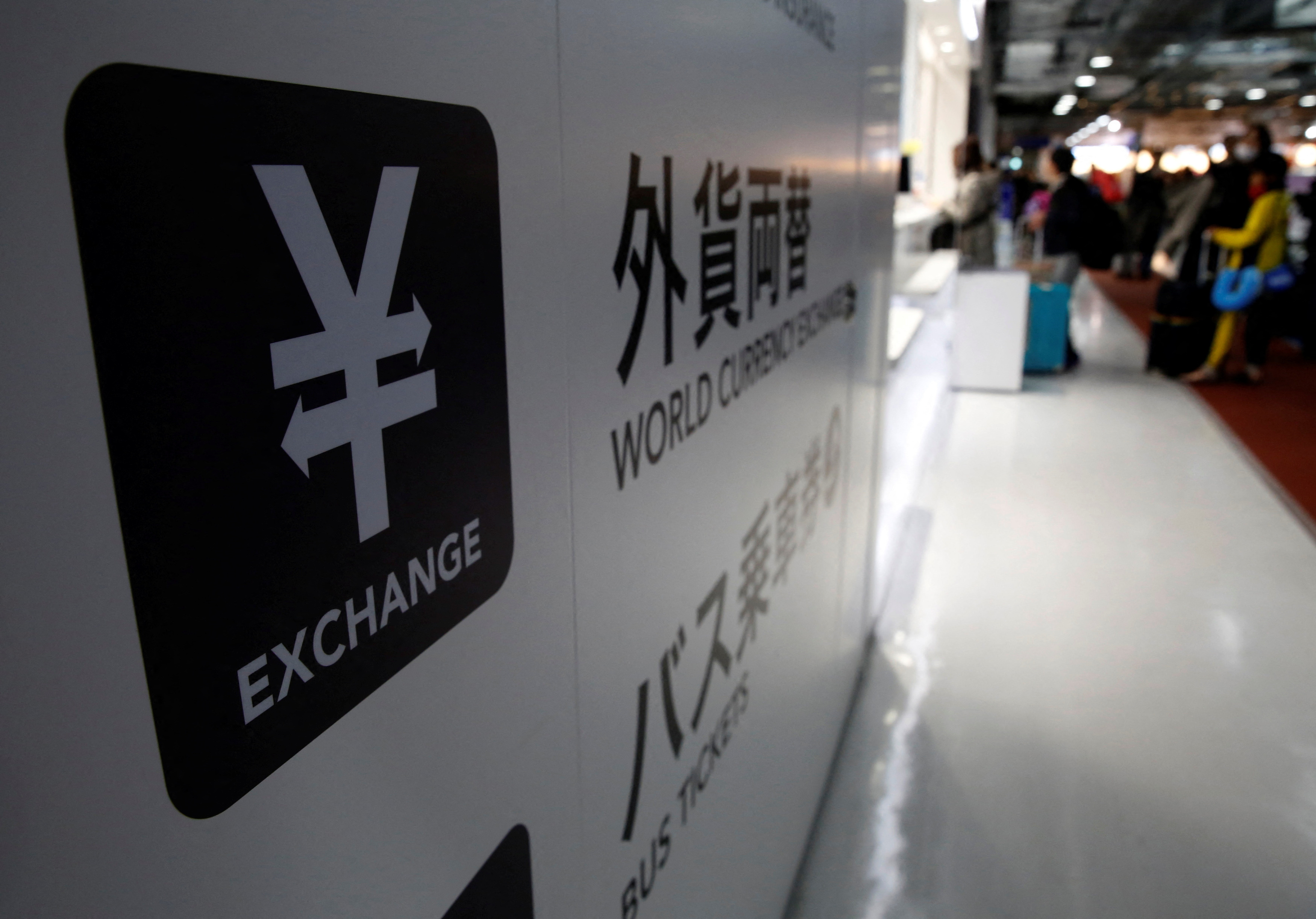 A Japanese Yen currency sign is seen at a currency exchange office as people line up to exchange money at Narita International airport