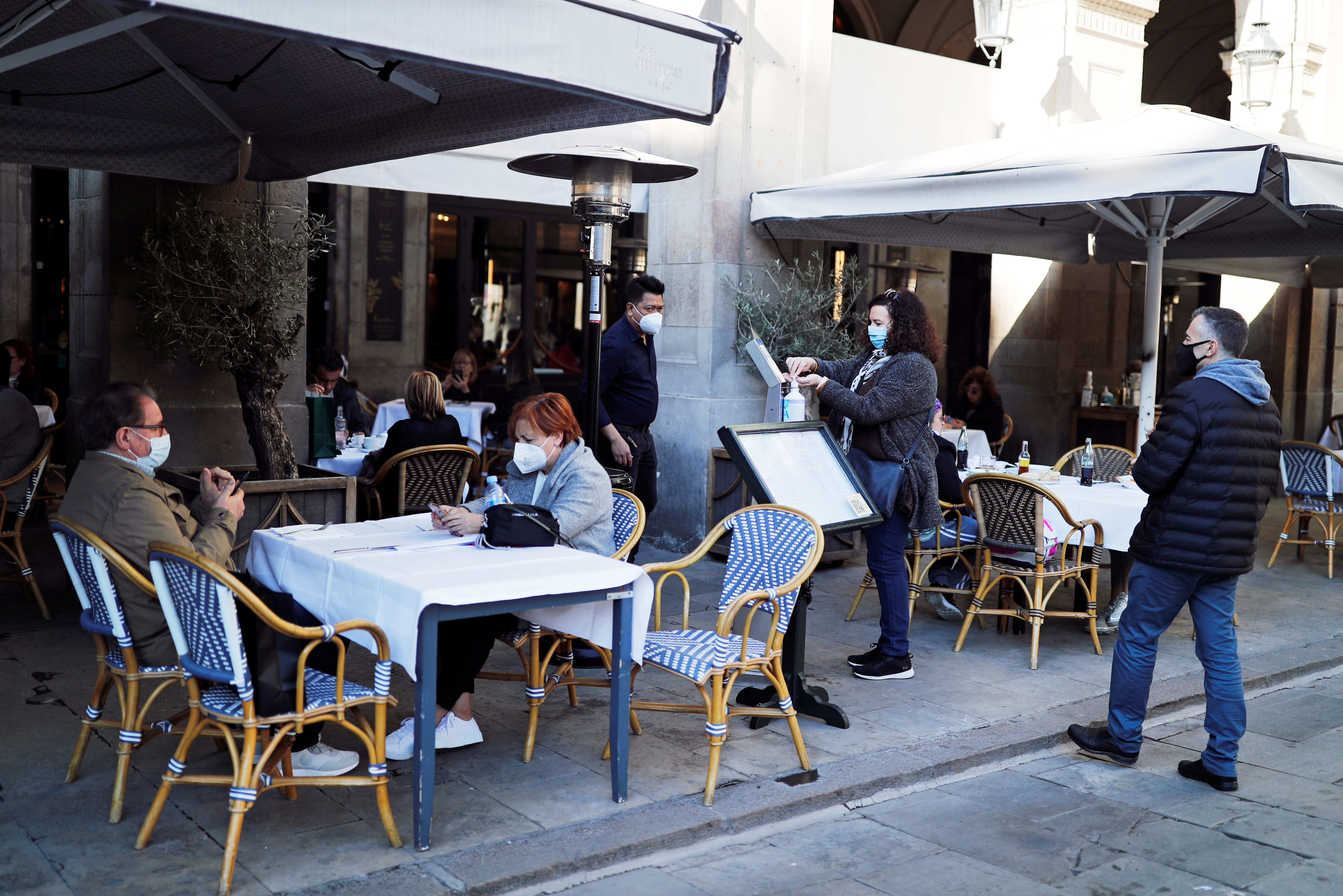 People wearing face masks sit at the terrace of the Les Quinze Nits restaurant on Real square, after Spain's Catalonia region allowed bars, restaurants, gyms and cinemas to reopen from Monday, gradually easing some of the restrictions put in place to tackle the coronavirus disease (COVID-19) outbreak, in Barcelona, Spain, November 23, 2020. REUTERS/Nacho Doce