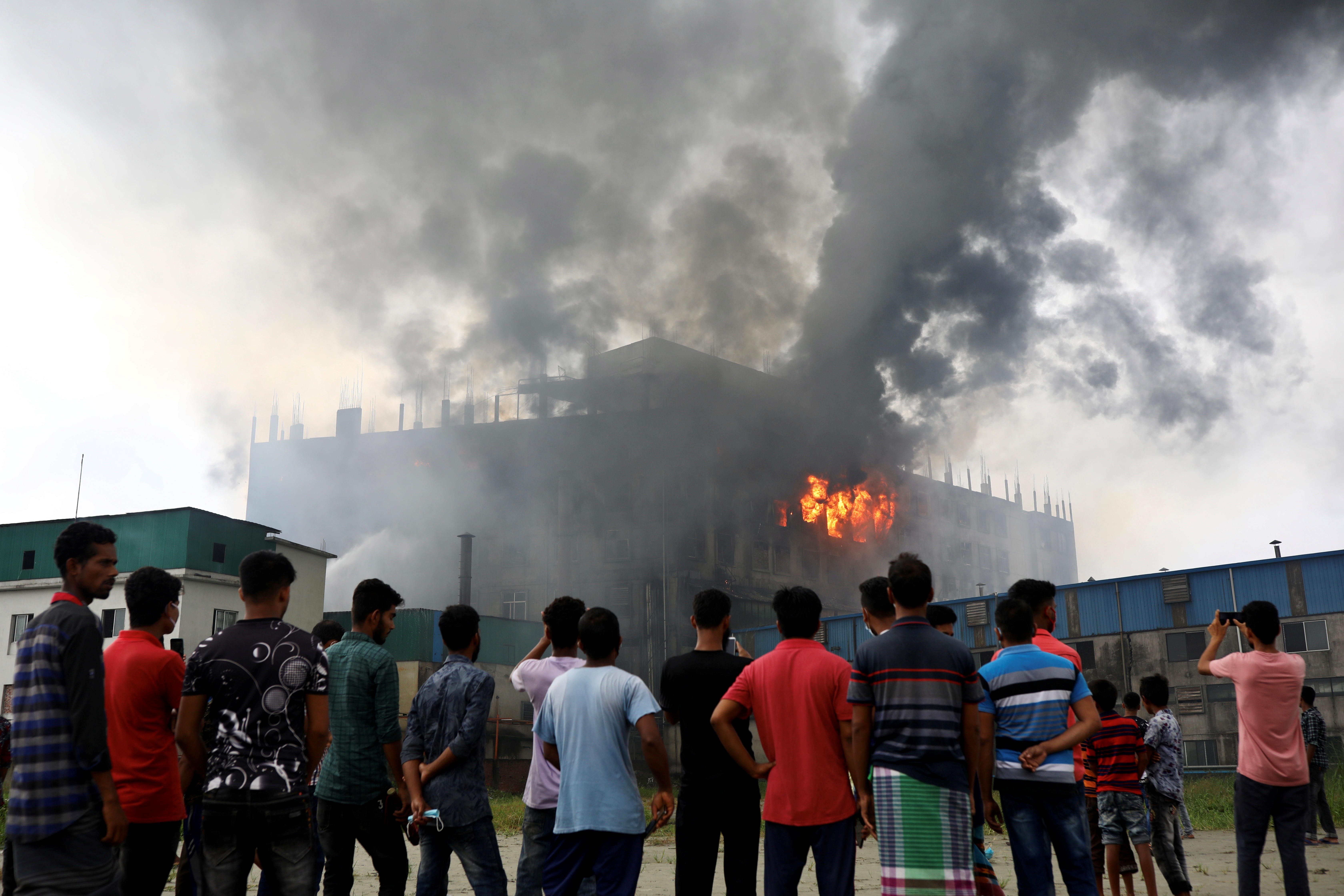 People look on as flames rise after a fire broke out at a Hashem Foods Ltd factory in Rupganj, Narayanganj district, on the outskirts of Dhaka, Bangladesh, July 9, 2021. REUTERS/Mohammad Ponir Hossain
