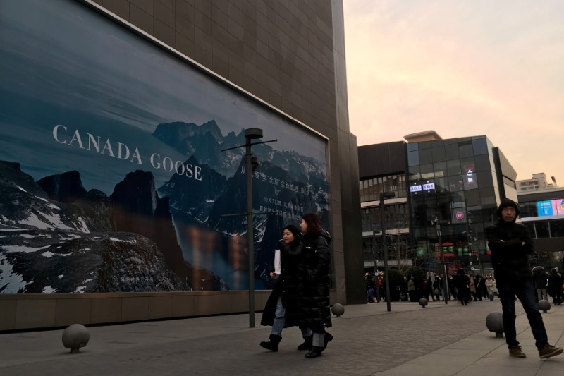People walk past an advertisement near the flagship store of Canadian luxury parka maker Canada Goose, in Sanlitun area of Beijing