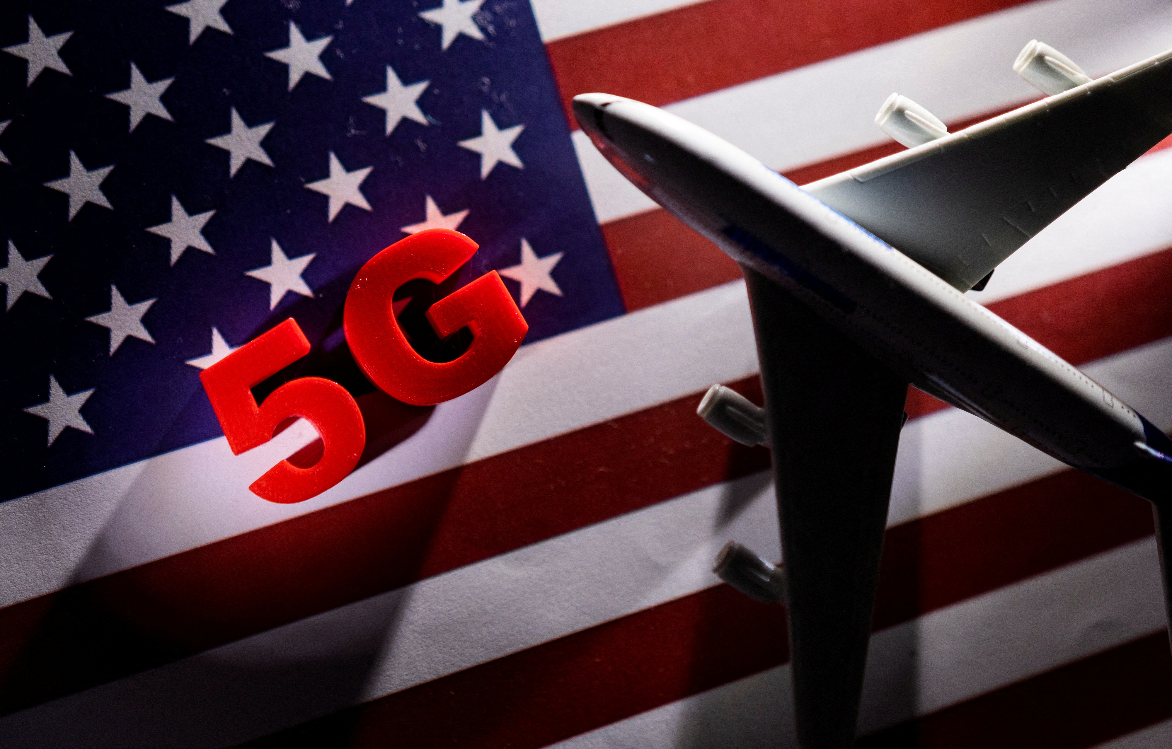 5G words and an airplane toy are placed on a printed U.S. flag in this illustration
