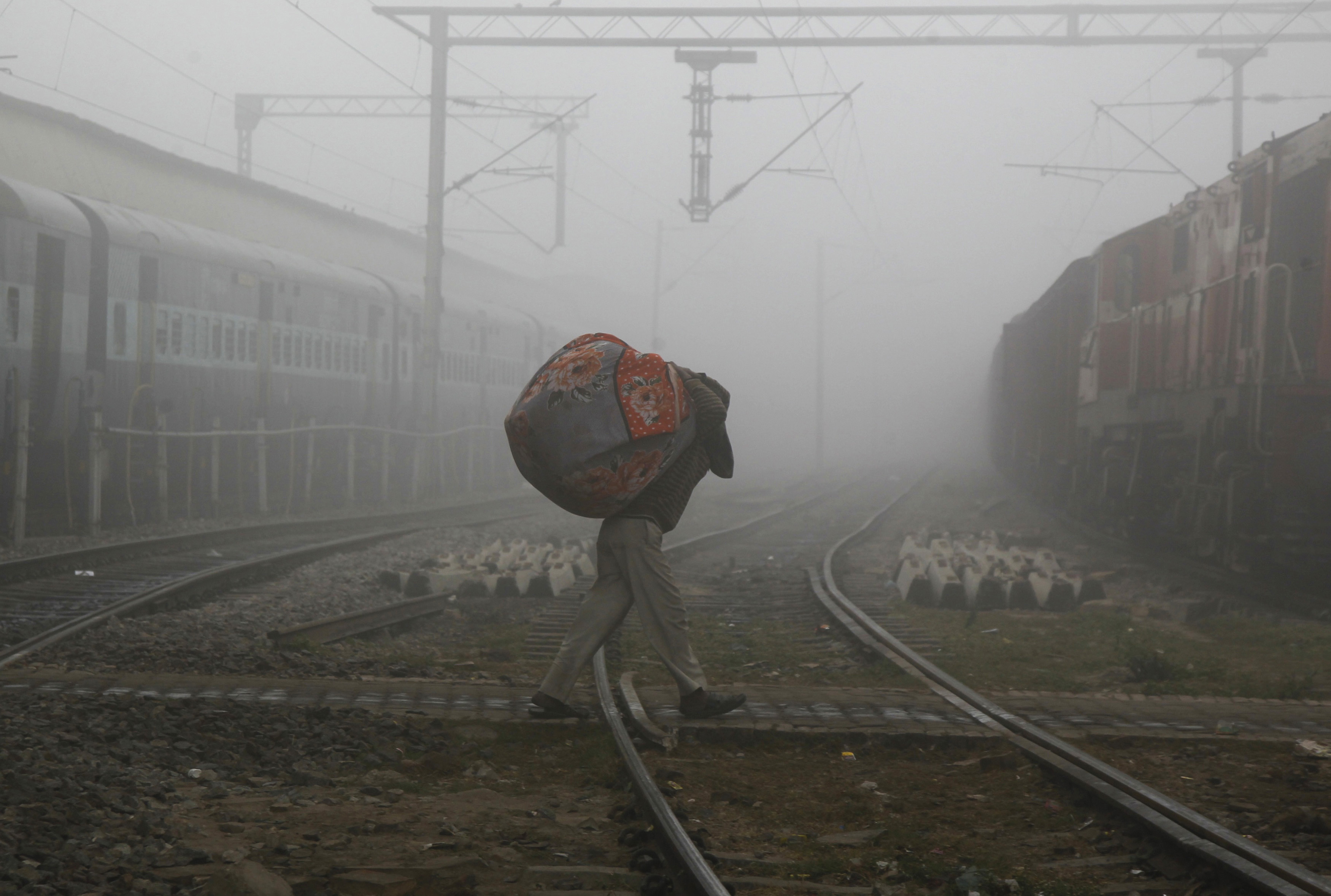 A man carries blankets as he crosses railway tracks on a foggy and cold winter morning in Allahabad