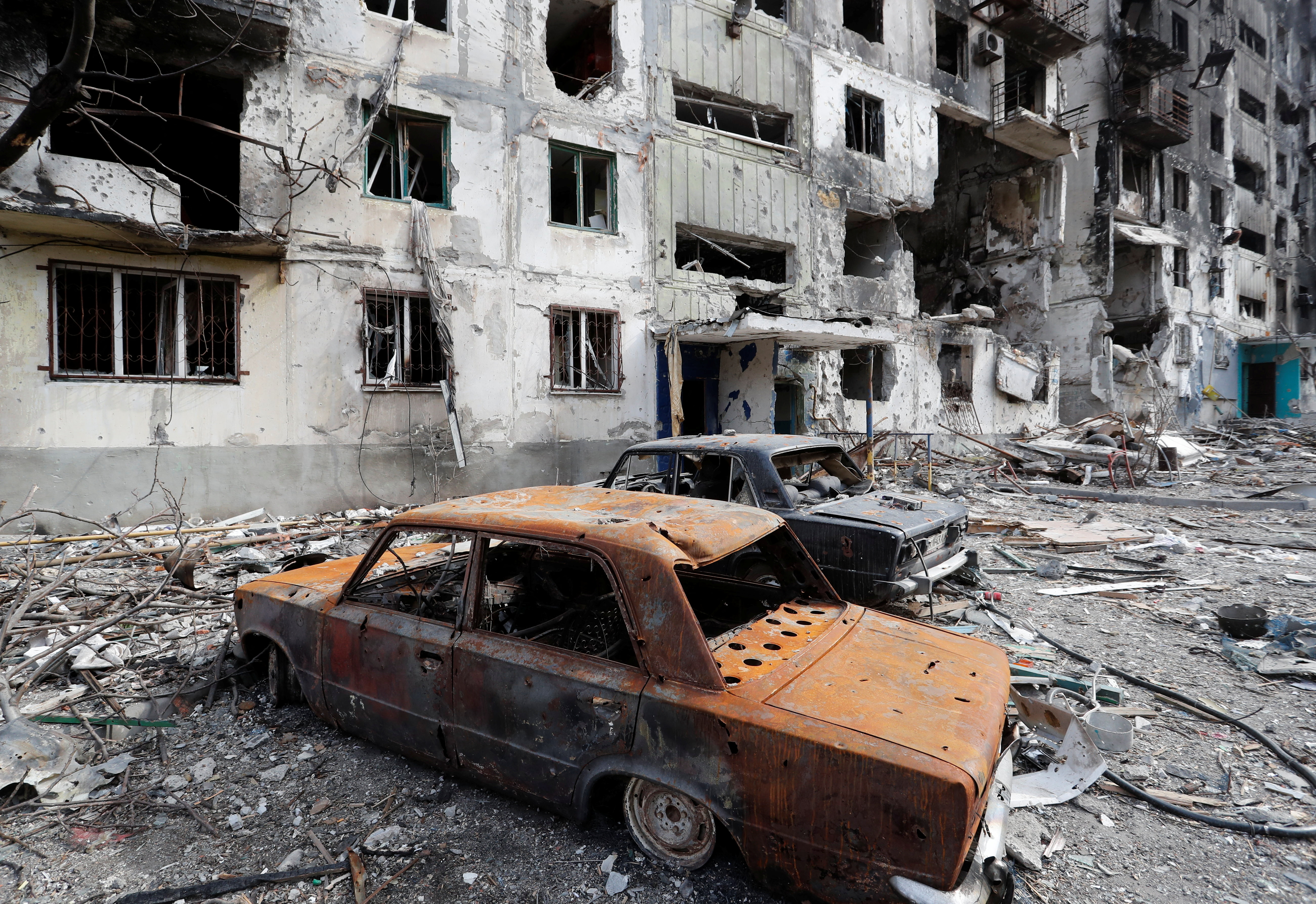 The remains of cars are seen in front of a destroyed apartment building in Mariupol