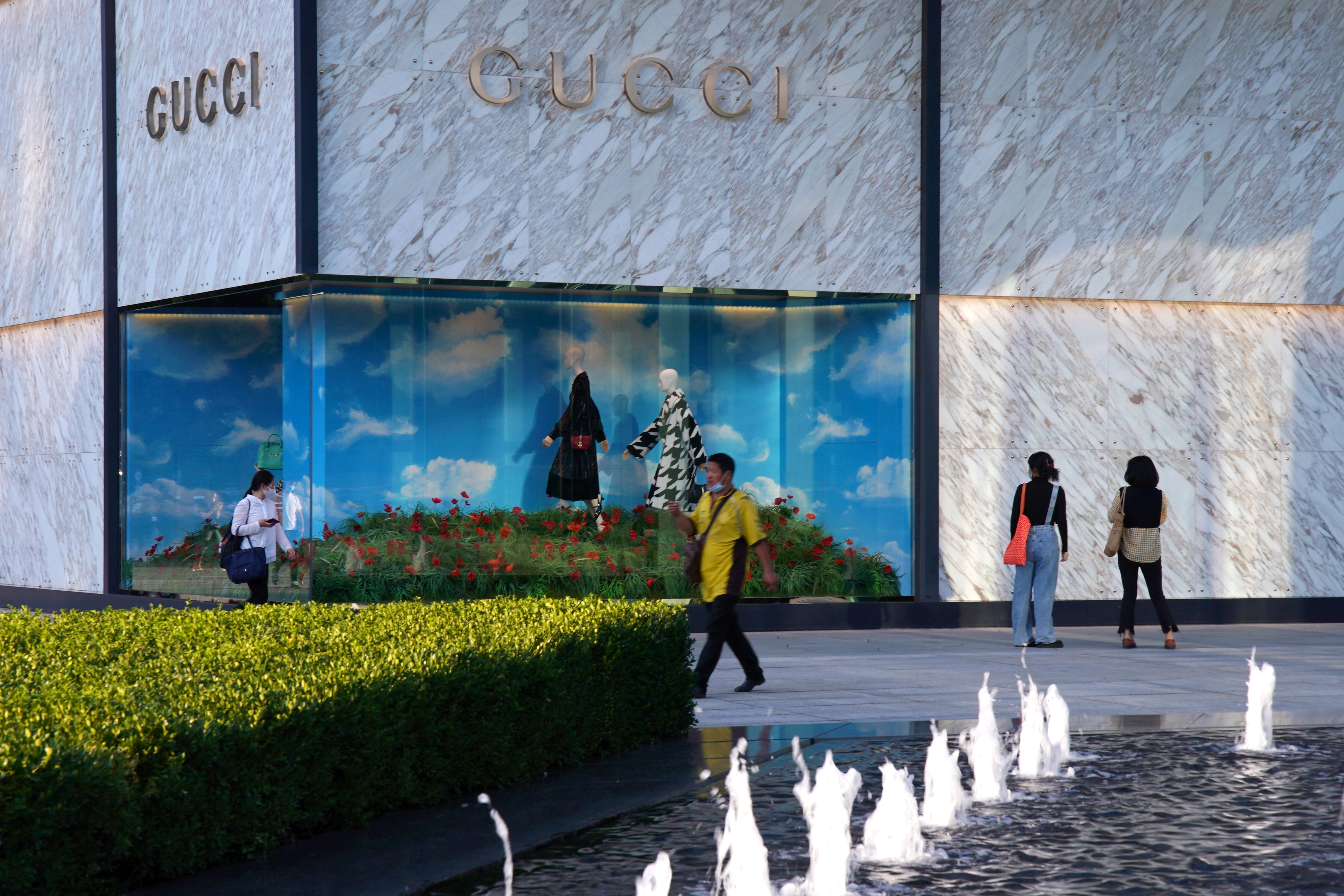 People wearing face masks following the COVID-19 outbreak walk past a store of Italian luxury brand Gucci at a shopping complex in Beijing
