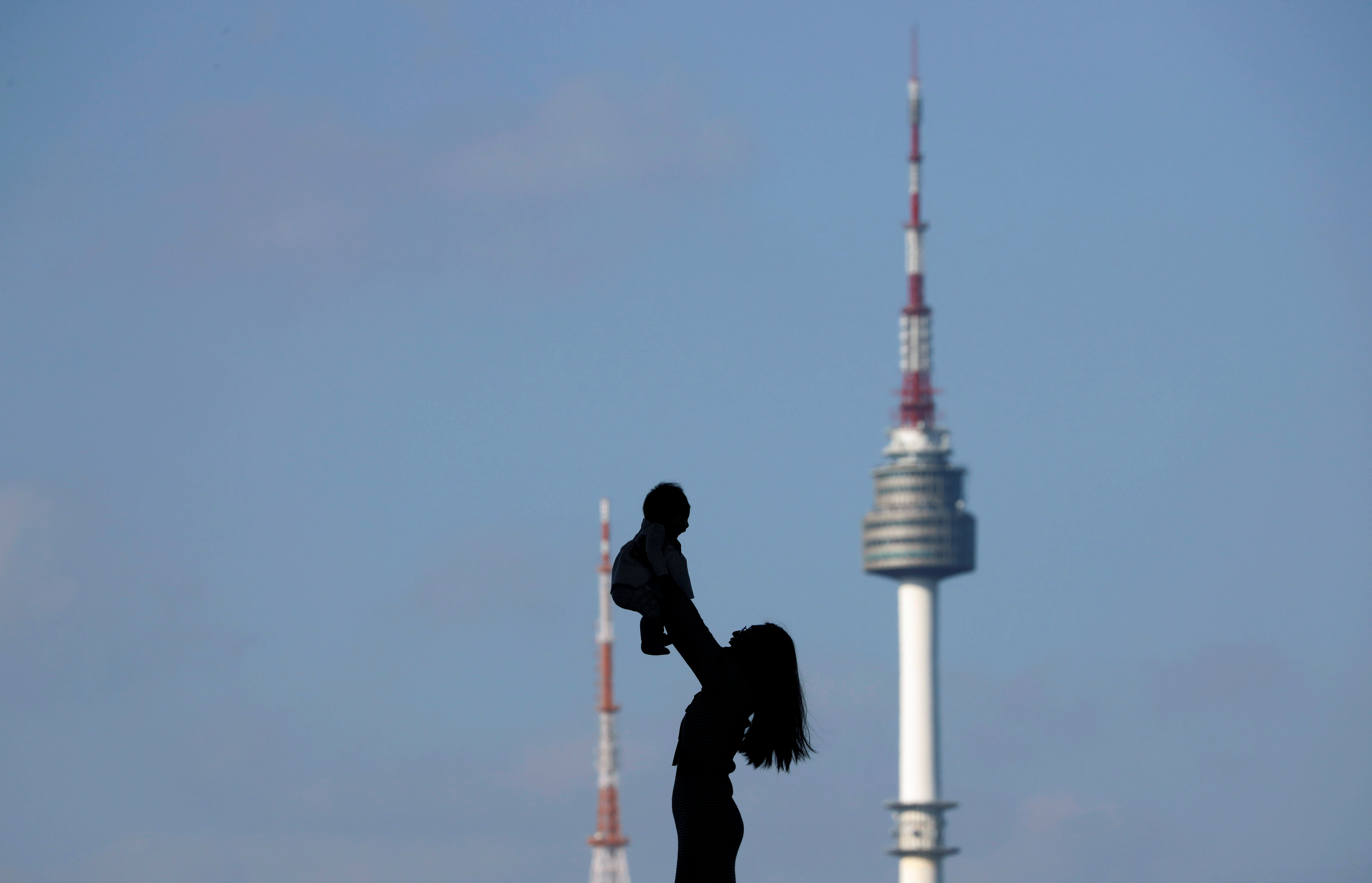 A woman holding up her baby is silhouetted against the backdrop of N Seoul Tower in Seoul