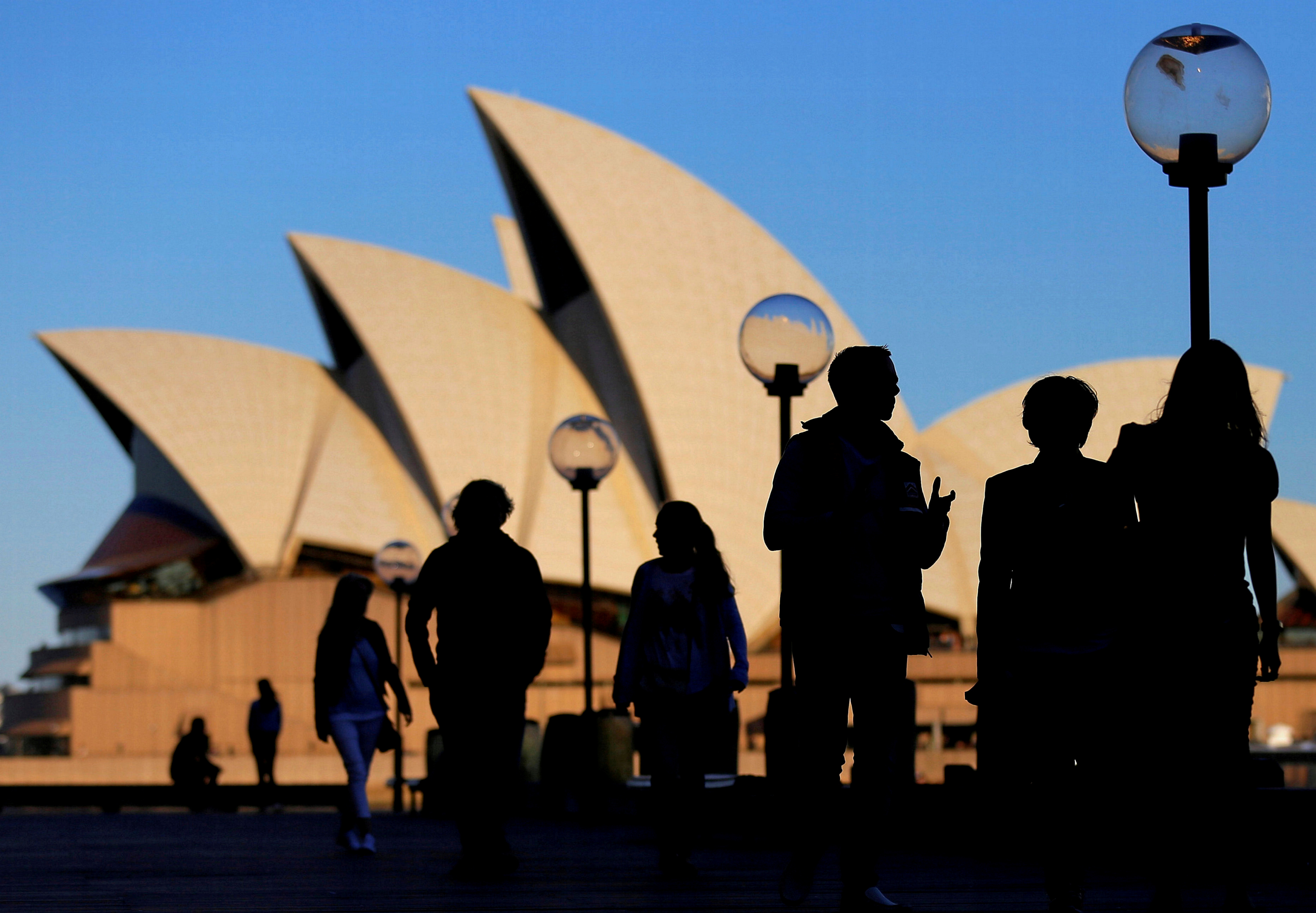 People are silhouetted against the Sydney Opera House at sunset in Australia
