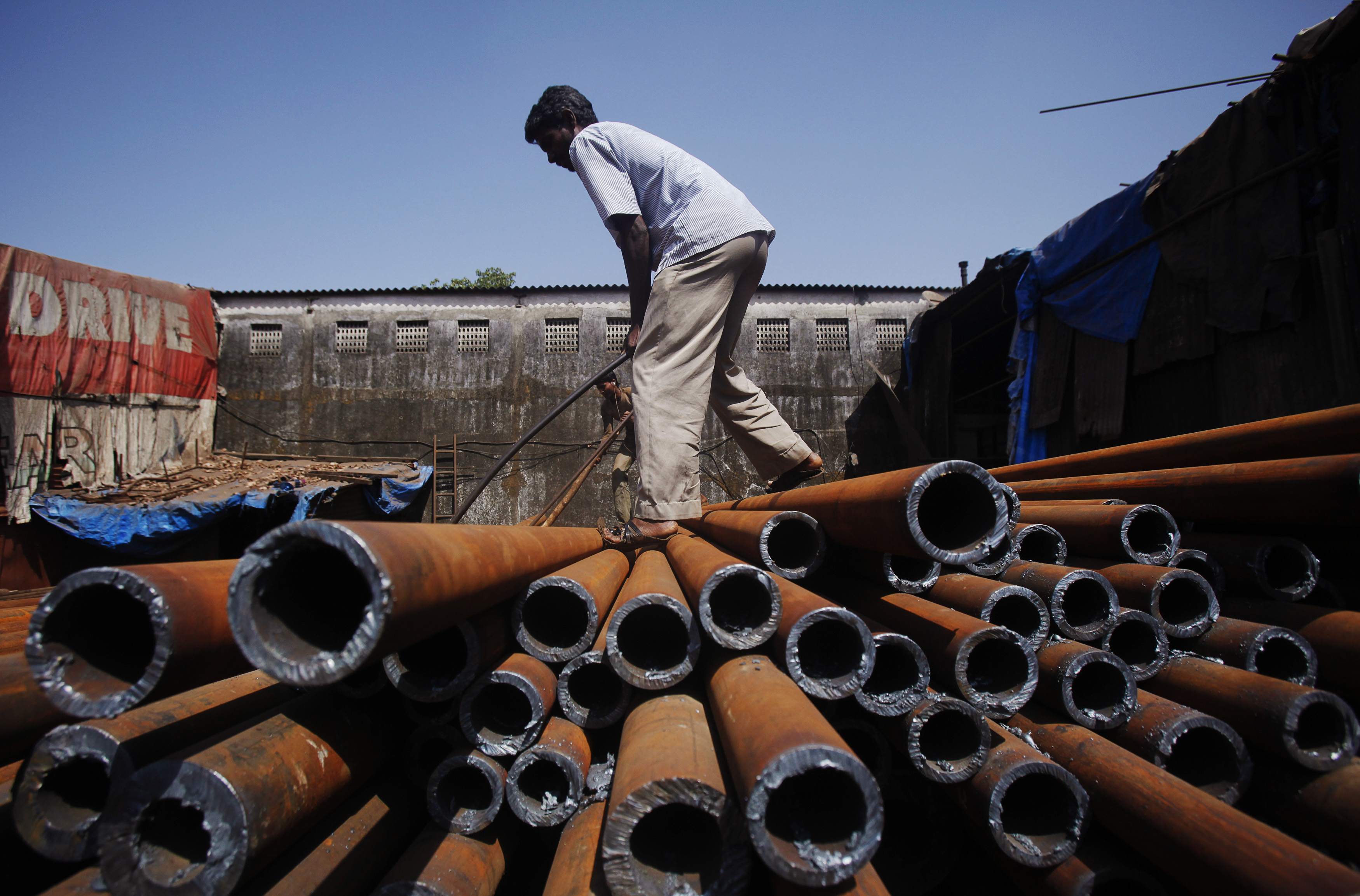 A worker moves iron pipes after unloading them at a factory in an industrial area in Mumbai