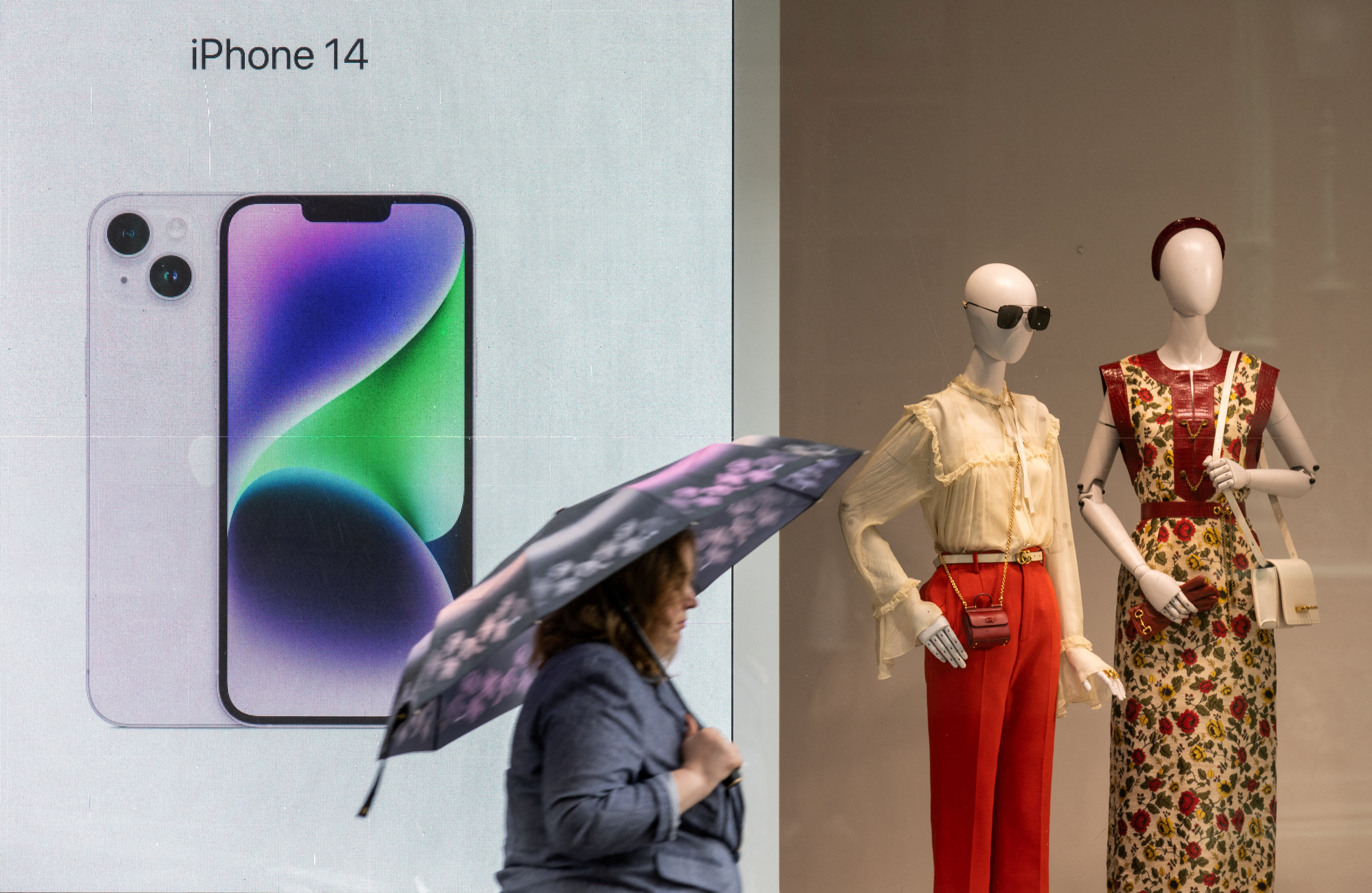 A woman with an umbrella walks past a display advertising Apple iPhone 14 during rainy weather in Moscow