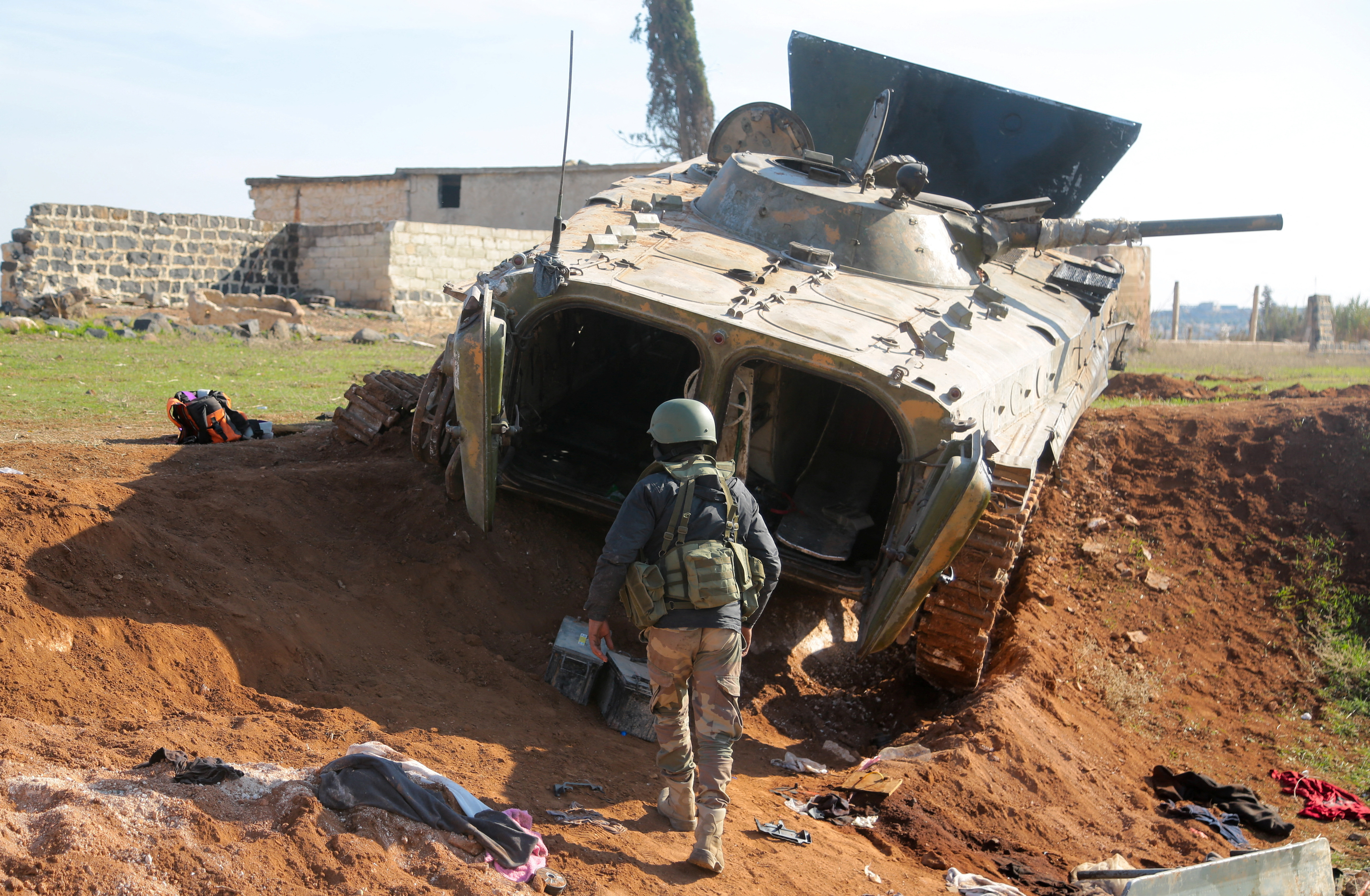 A rebel fighter walks near a military vehicle in Menagh